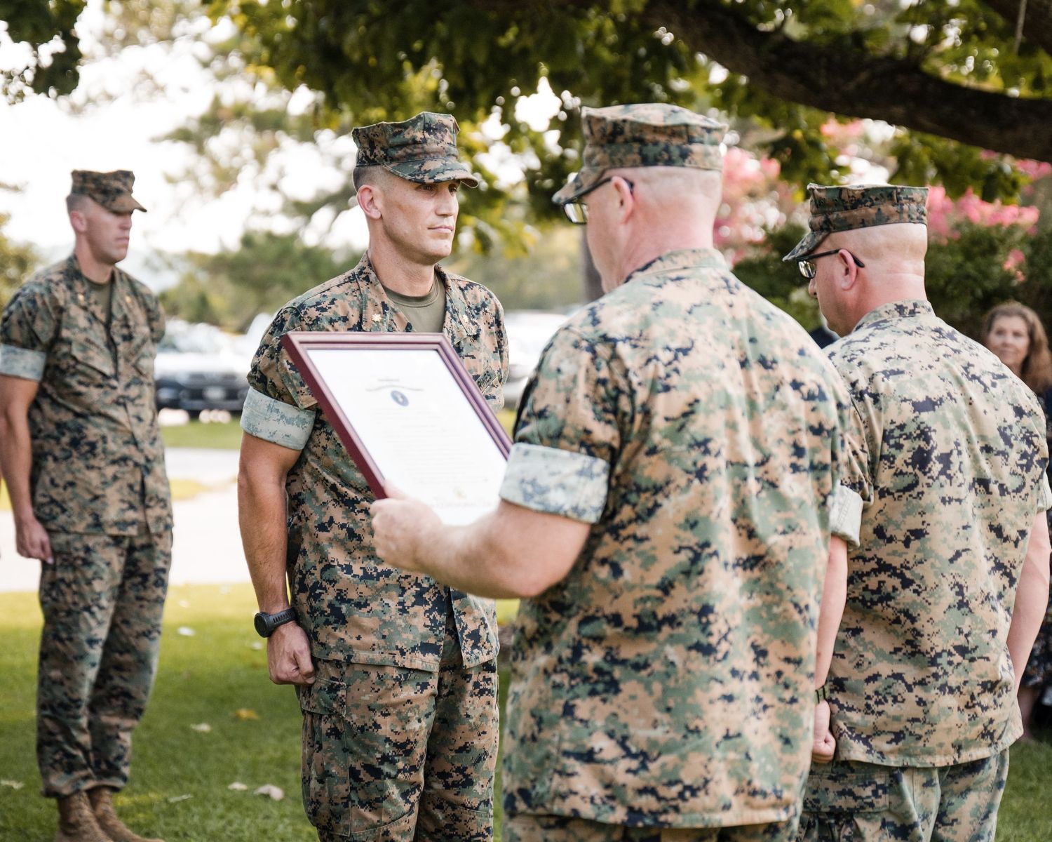 Military personnel in camouflage uniforms gather outdoors during a daytime event.