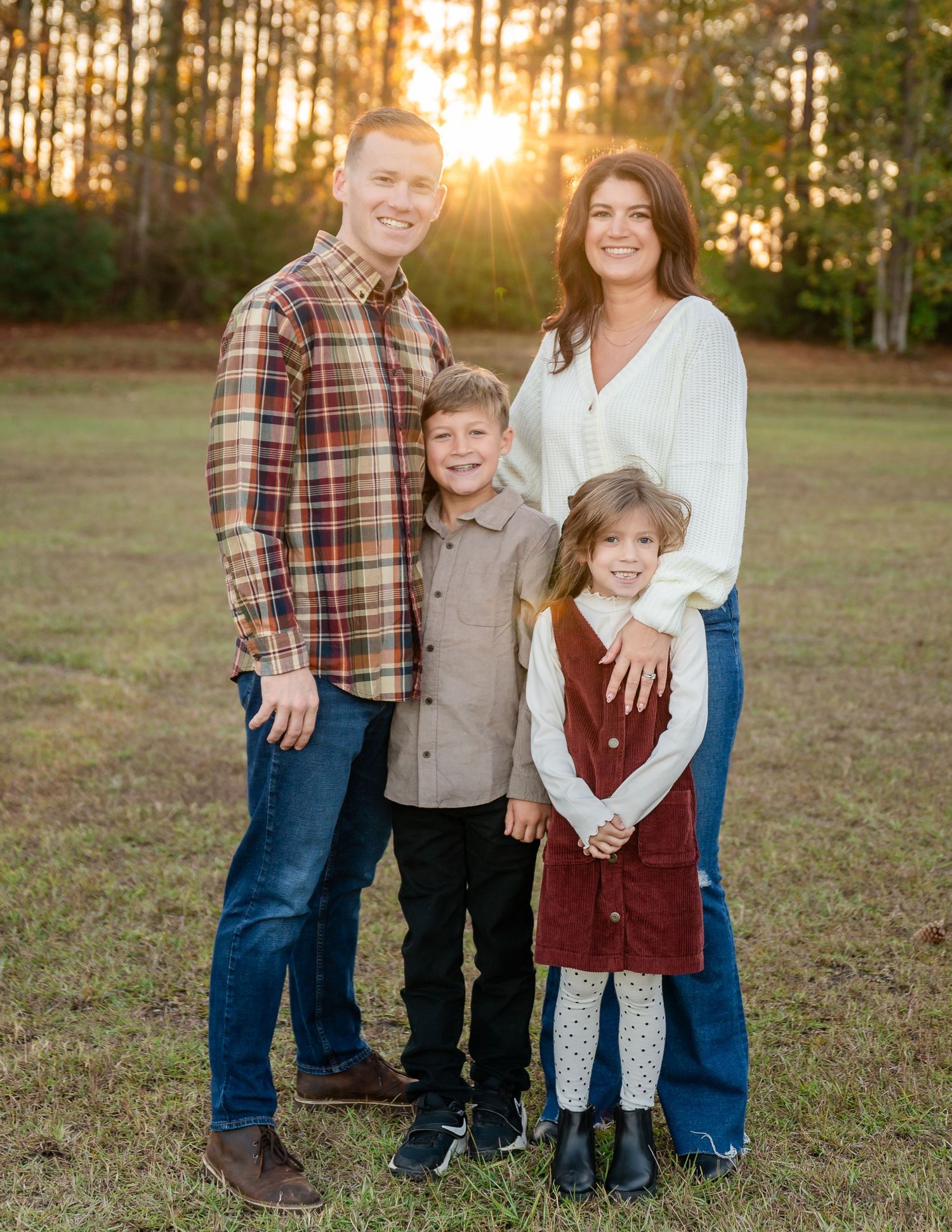 Casual family photo session in grassy field with pine trees at sunset.