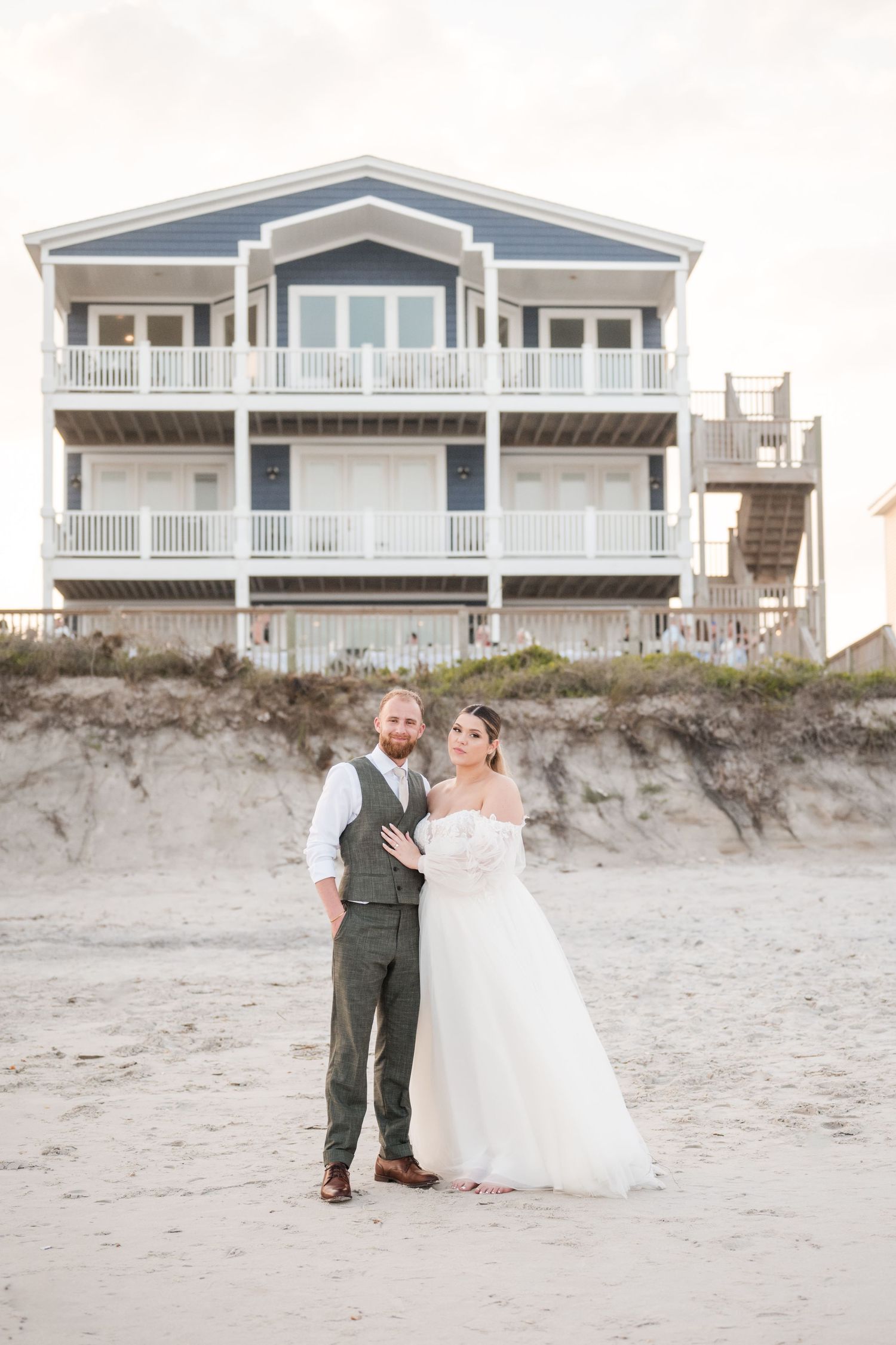 Beach wedding portraits with coastal homes in the background at sunset.