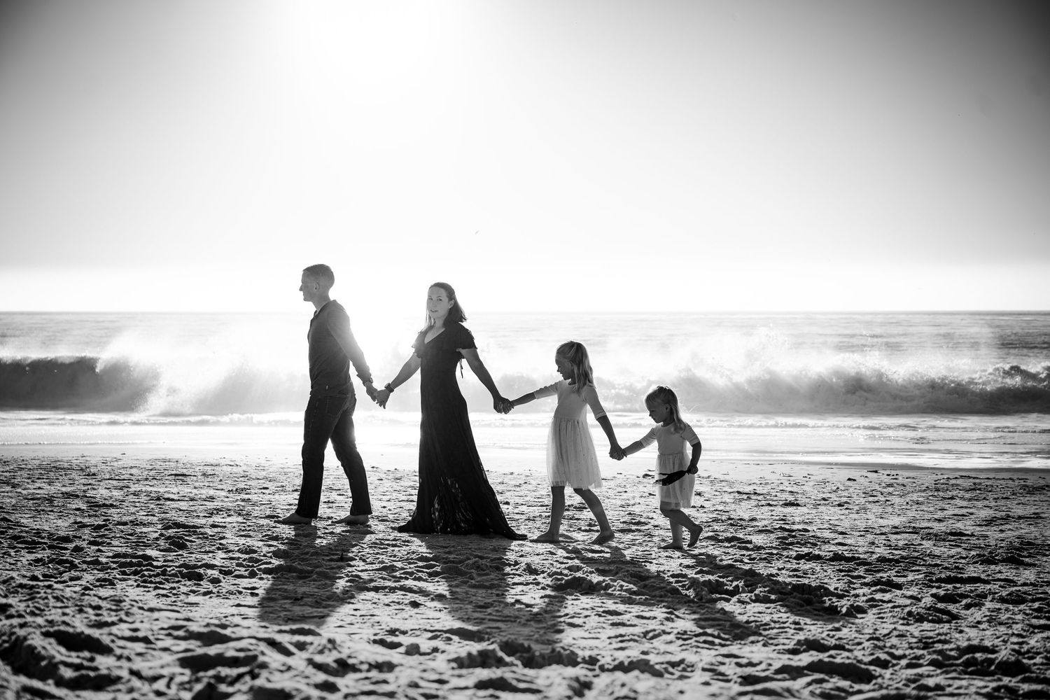 Family silhouettes walking together along misty beach at sunset.