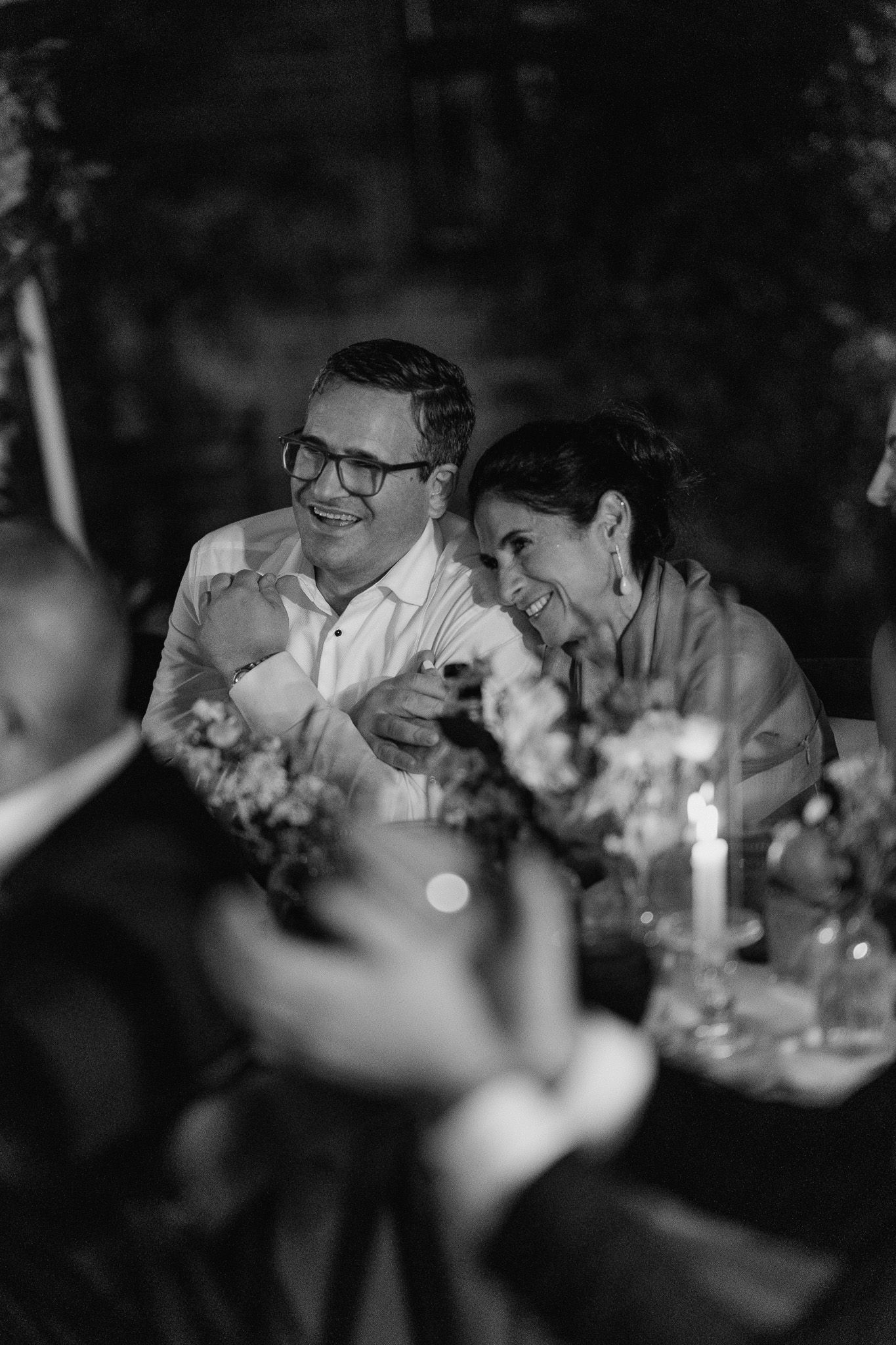 A candid black and white photo of two guests laughing together during an evening reception dinner.