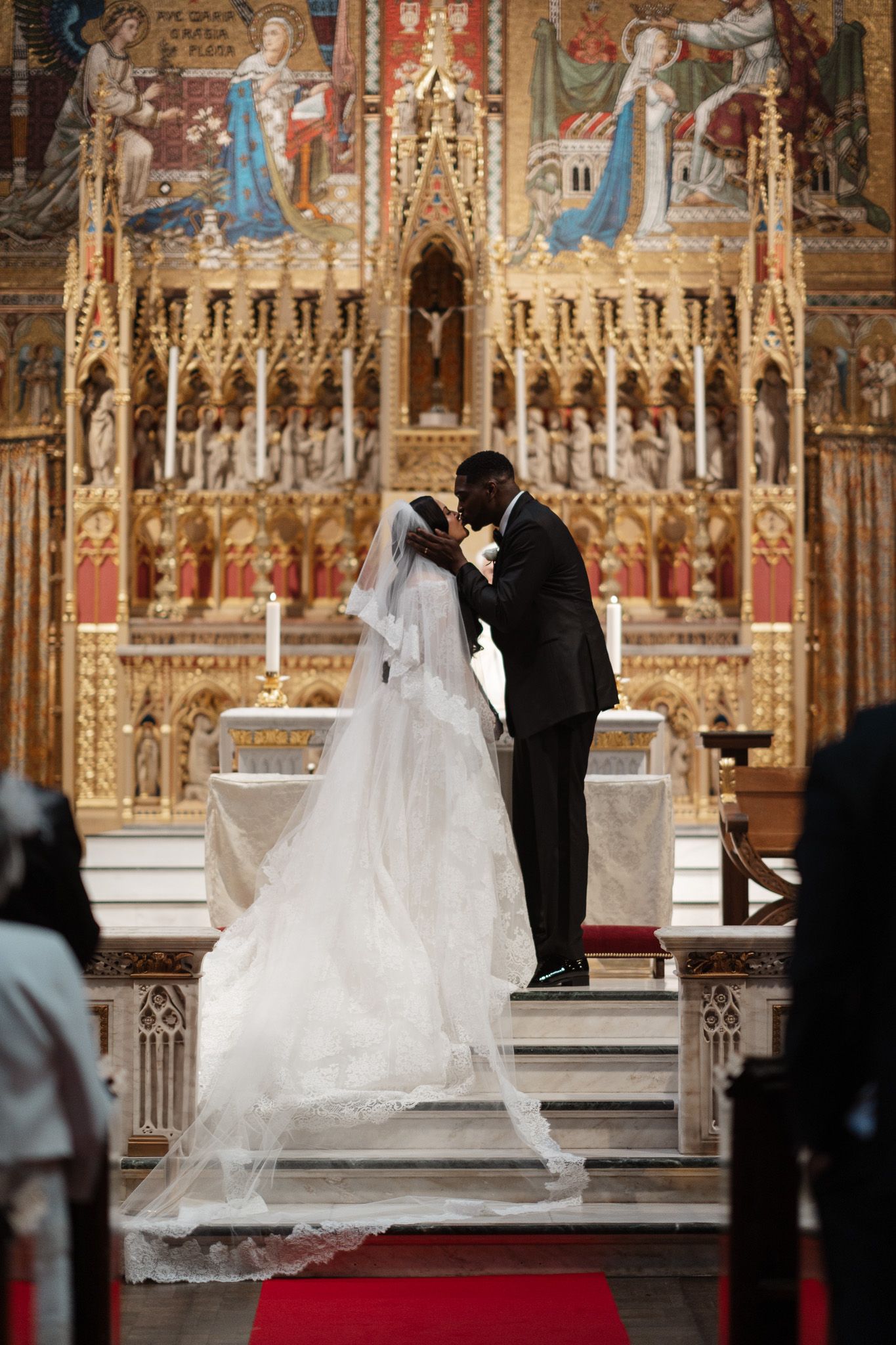 A silhouette of a couple sharing their first kiss at the altar of an ornate church with gothic architecture.