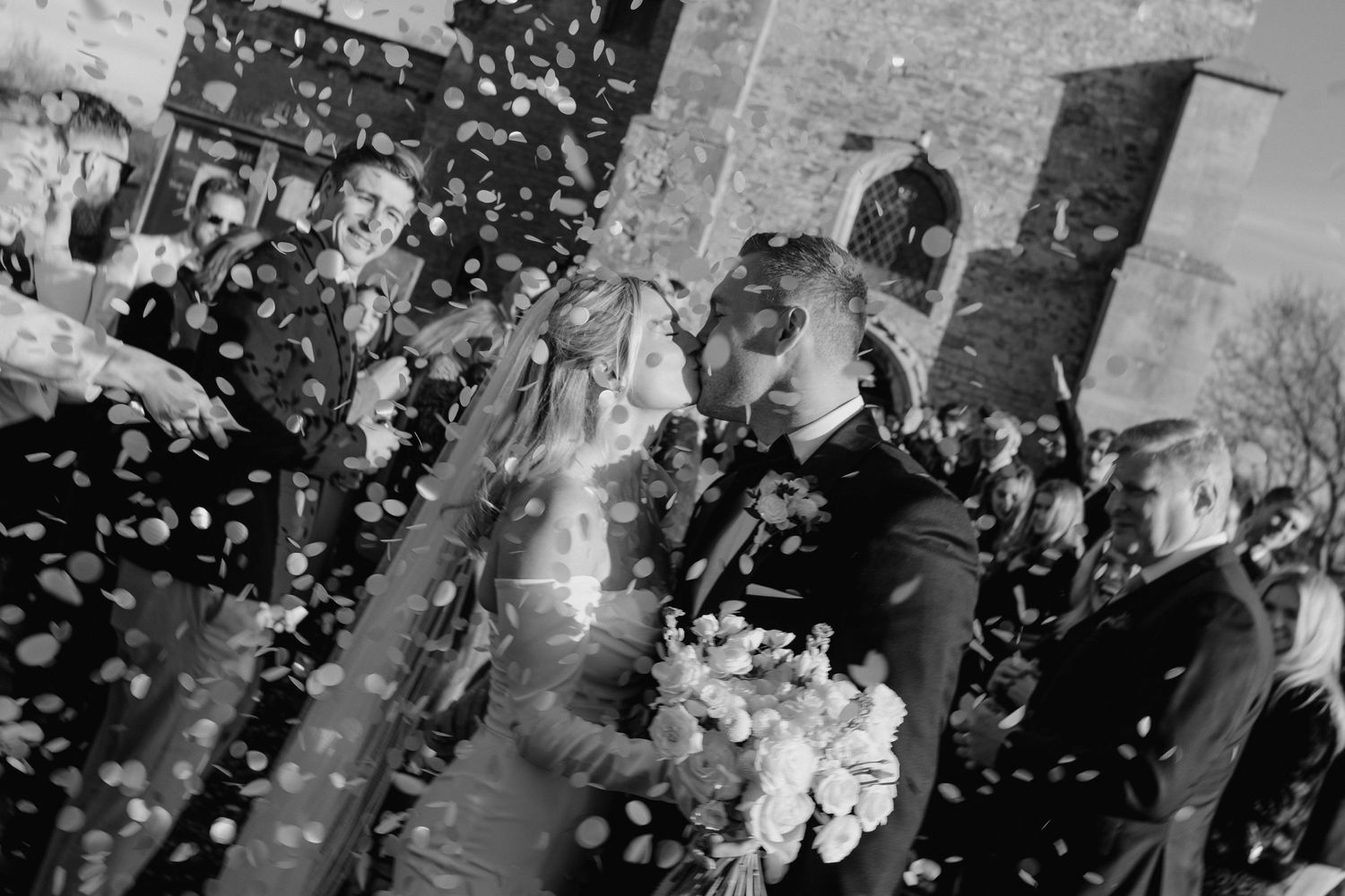 A black and white wedding photo with confetti falling around celebrating newlyweds.
