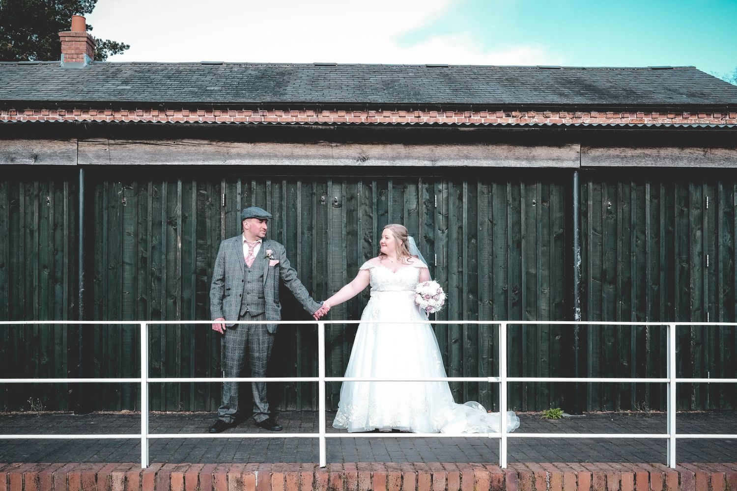 Bride and groom holding hands in front of a rustic wooden barn on their wedding day.