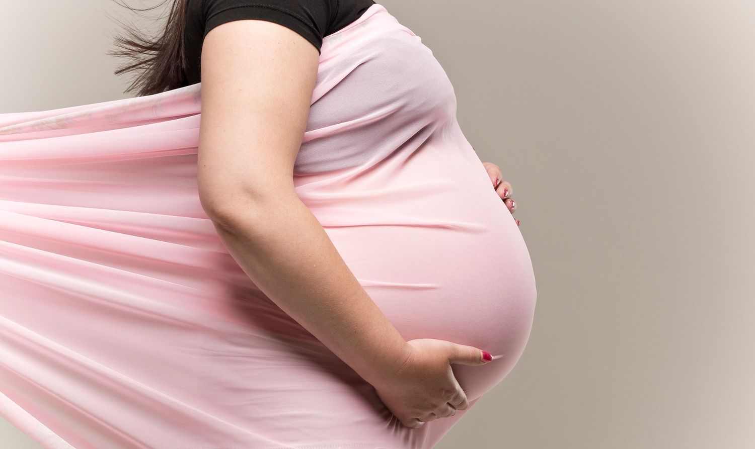 Pregnant woman in pink dress cradling her baby bump, showcasing a beautiful maternity moment.