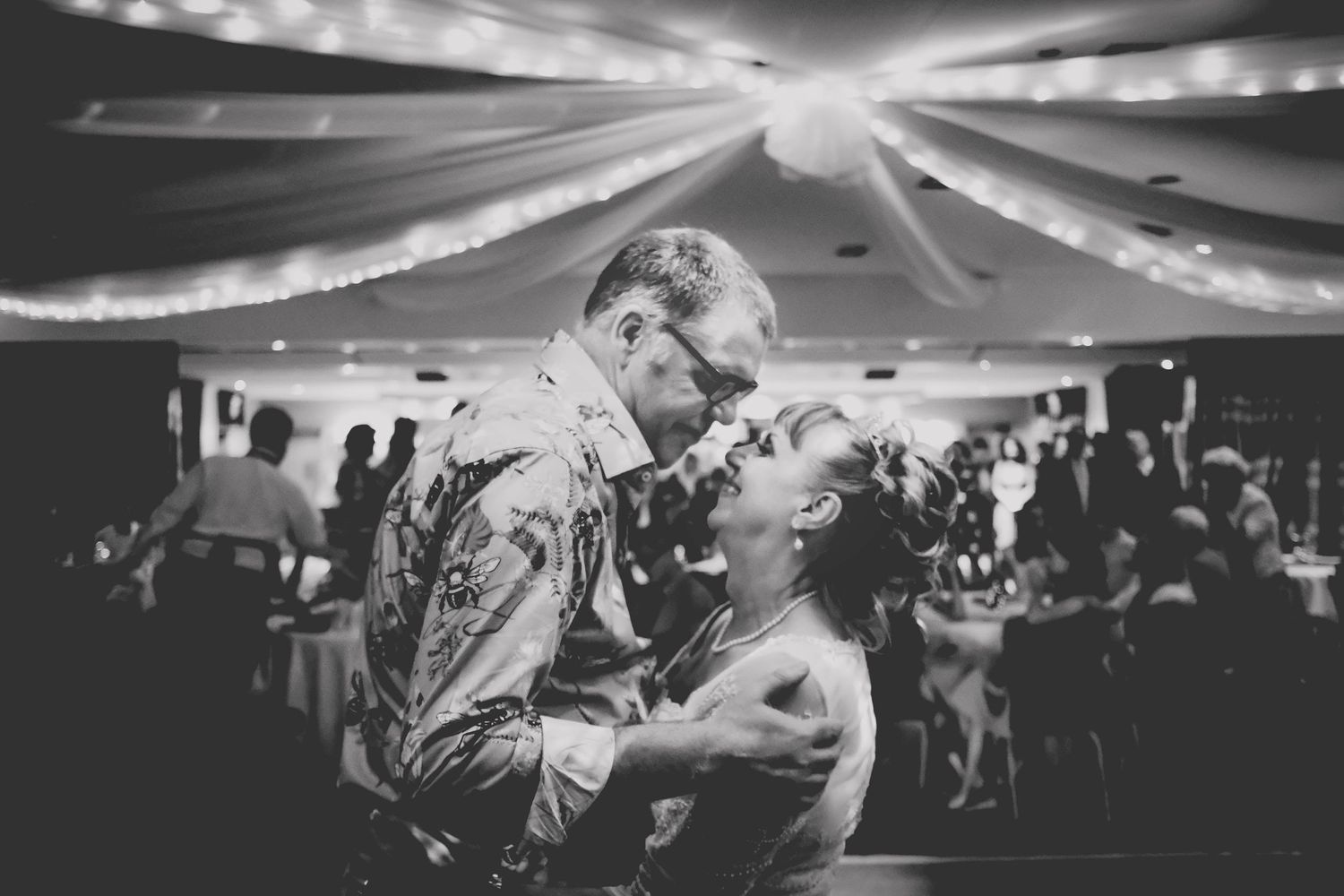Black and white photo of a couple sharing an intimate dance at a wedding reception with string lights overhead.