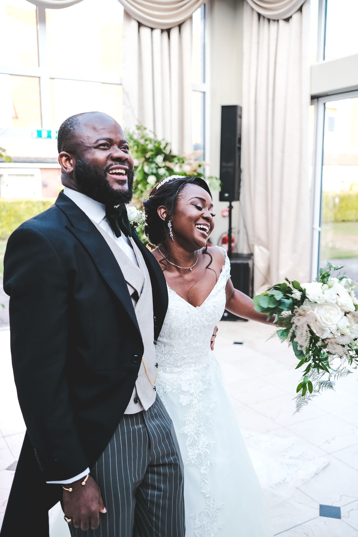 Joyful Black bride and groom laughing together on their wedding day, bride holding white bouquet.