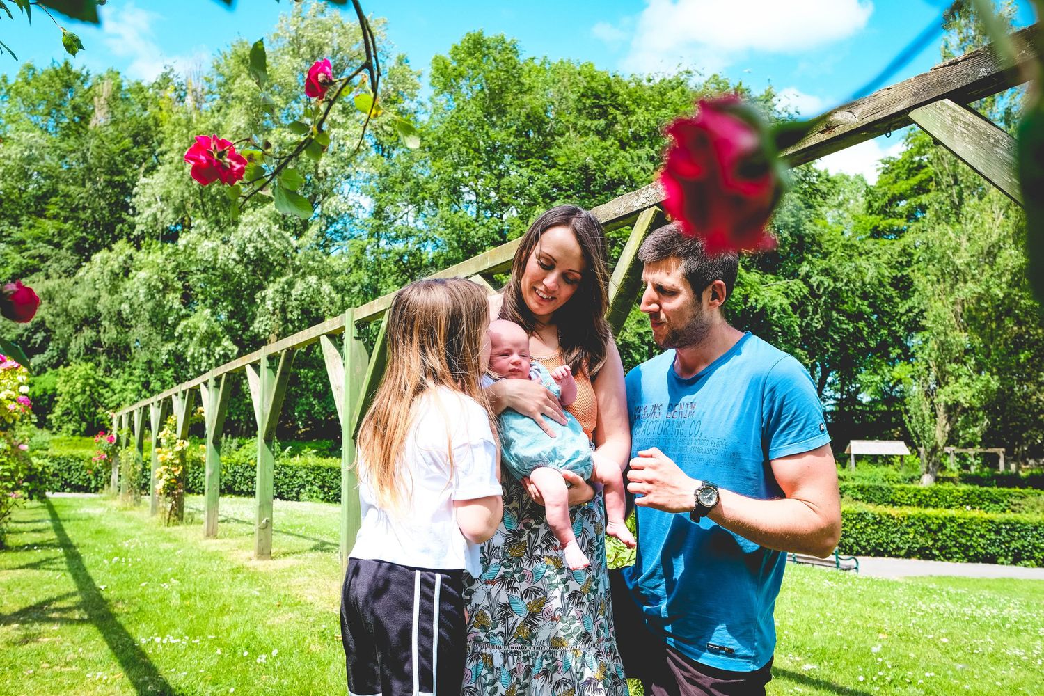 A happy family with a baby enjoys a sunny garden with roses and green hedges on a bright summer day.