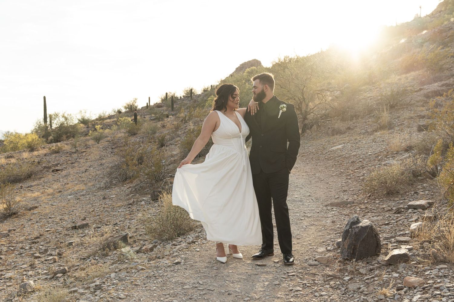 Couple walking hand in hand through a desert landscape at sunset with mountains in the background.
