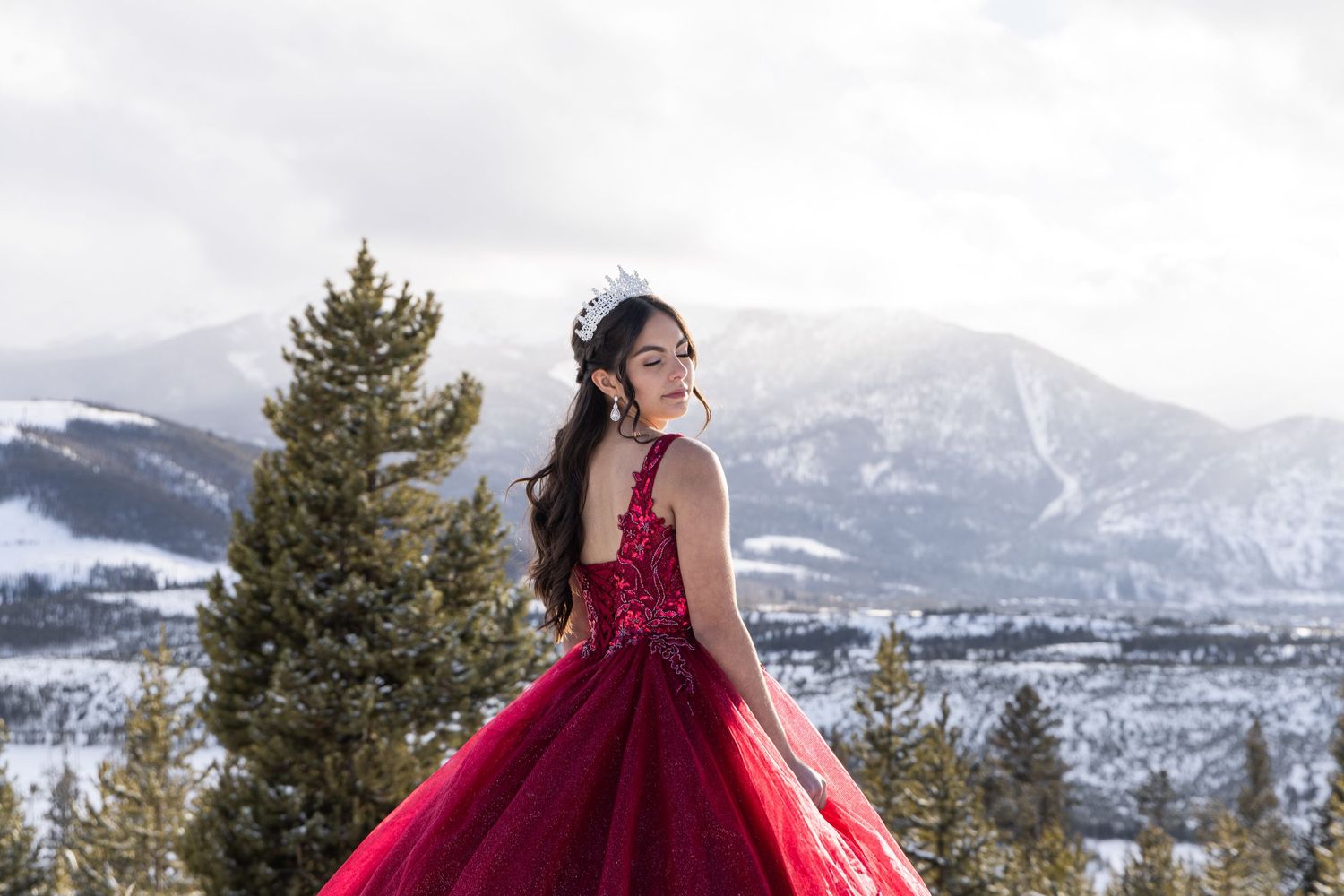 A red formal gown against a snowy mountain backdrop with evergreen trees in the winter landscape.