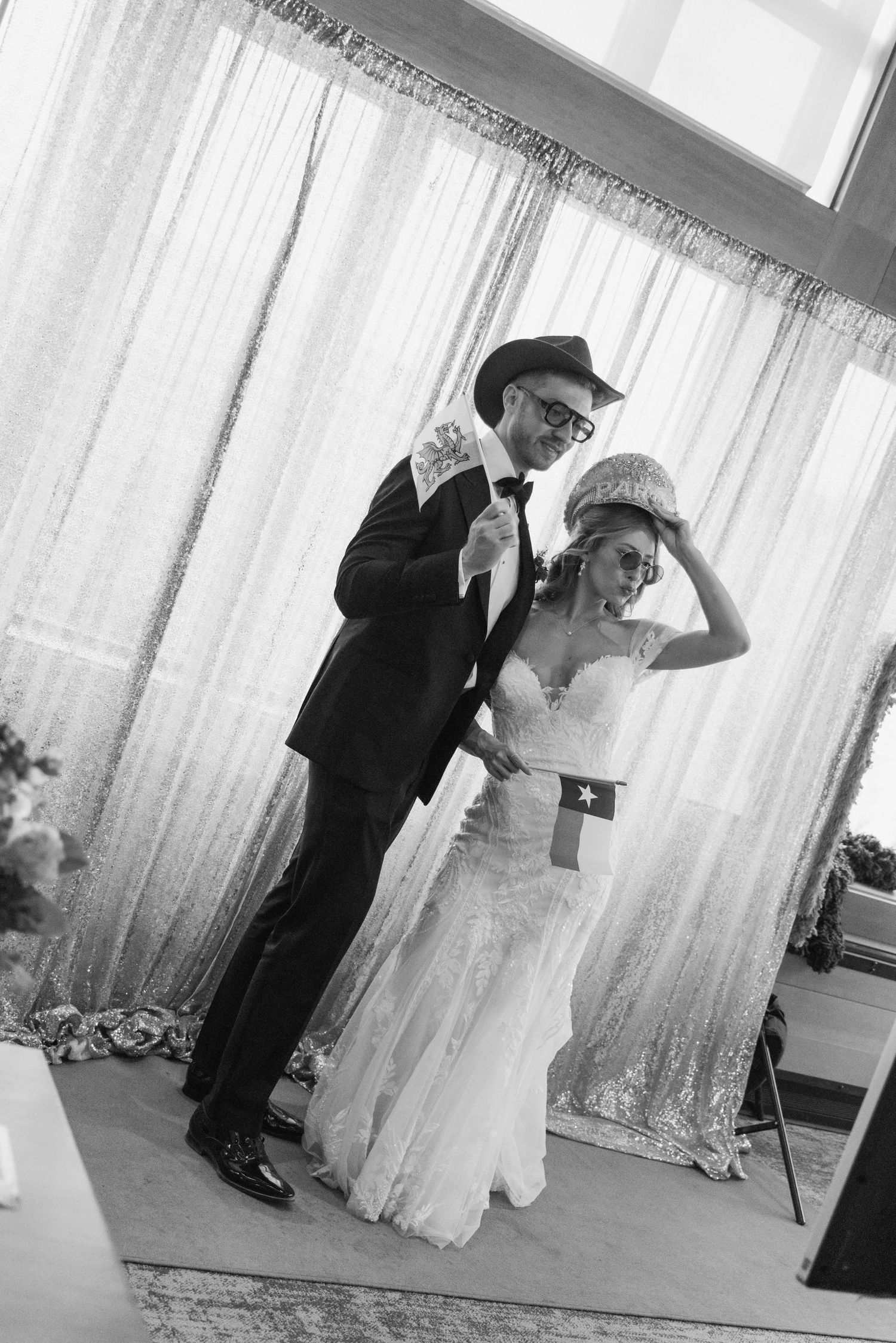 Black and white photo of a bride and groom dancing together at their wedding reception, wearing stylish hats.