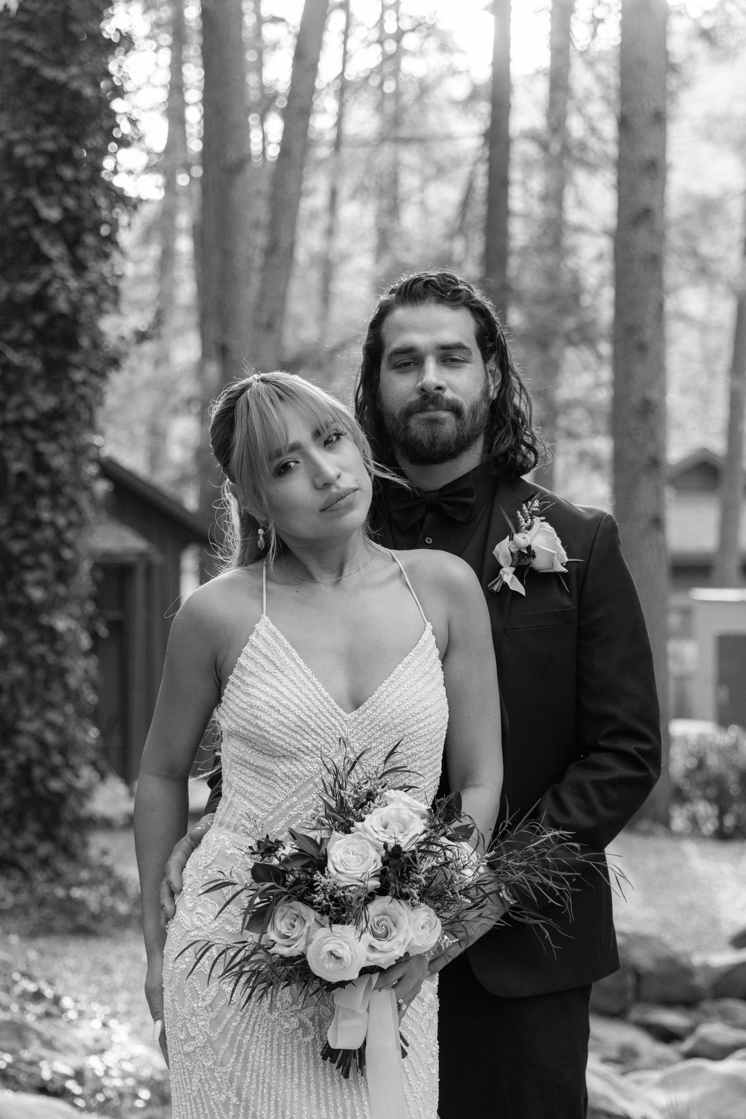 A romantic black and white wedding photo series showing a couple posing together in a wooded outdoor setting.