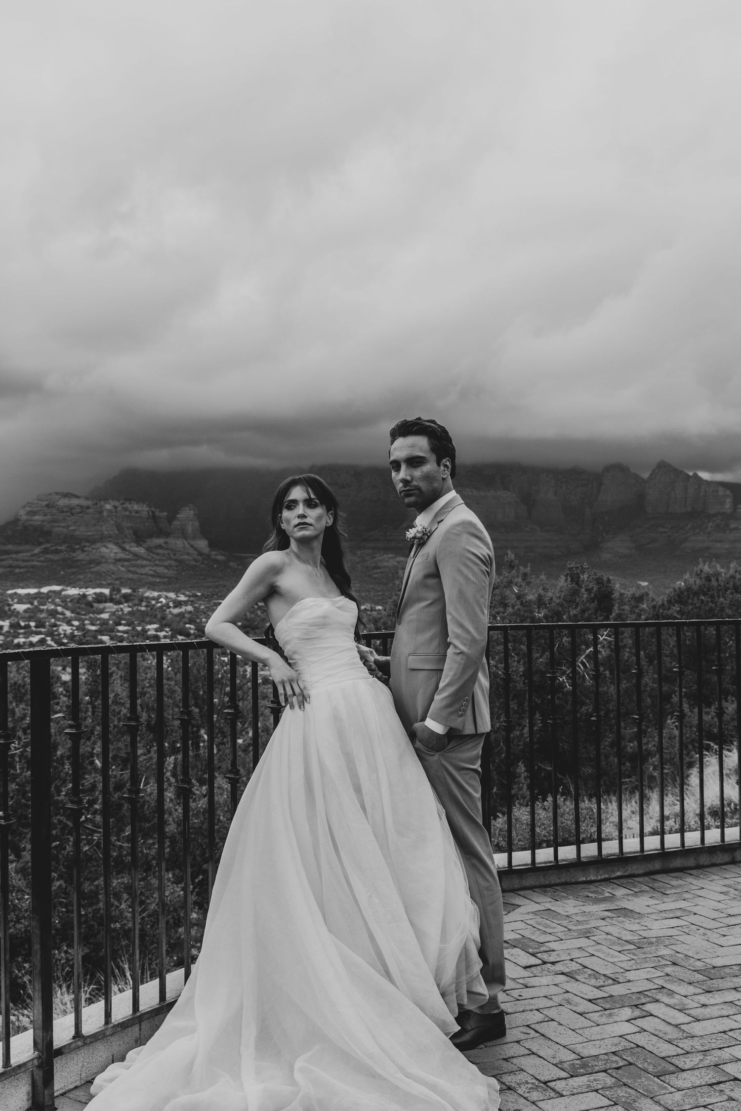 Newlywed couple shares romantic moments at a scenic mountain overlook with dramatic cloudy skies and city views below.