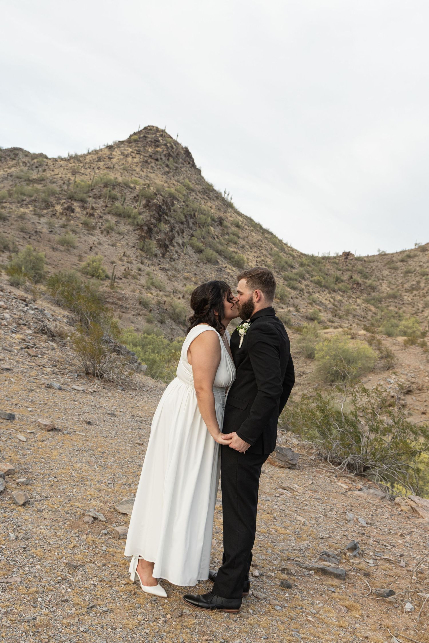 A couple shares a romantic kiss against a desert mountain backdrop in a wedding ceremony.