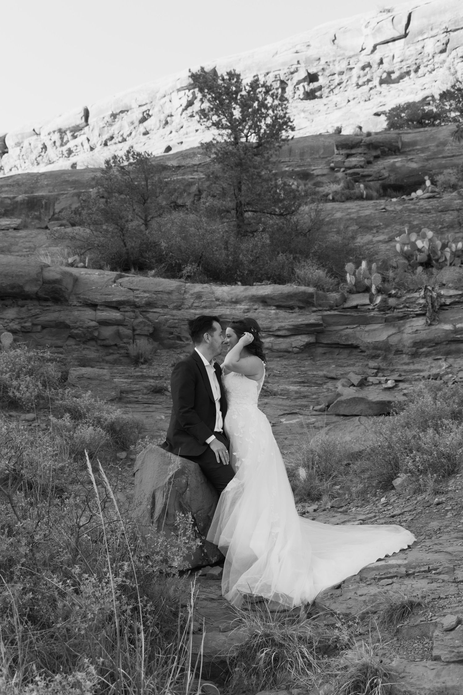 Bride and groom share a romantic kiss on rocky desert terrain in black and white wedding portrait.
