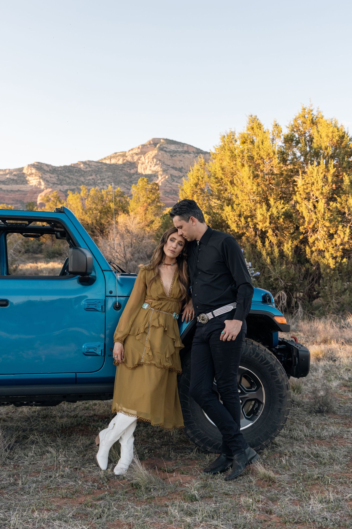 A romantic autumn scene of a couple standing beside a turquoise pickup truck with yellow aspen trees and mountains in background.