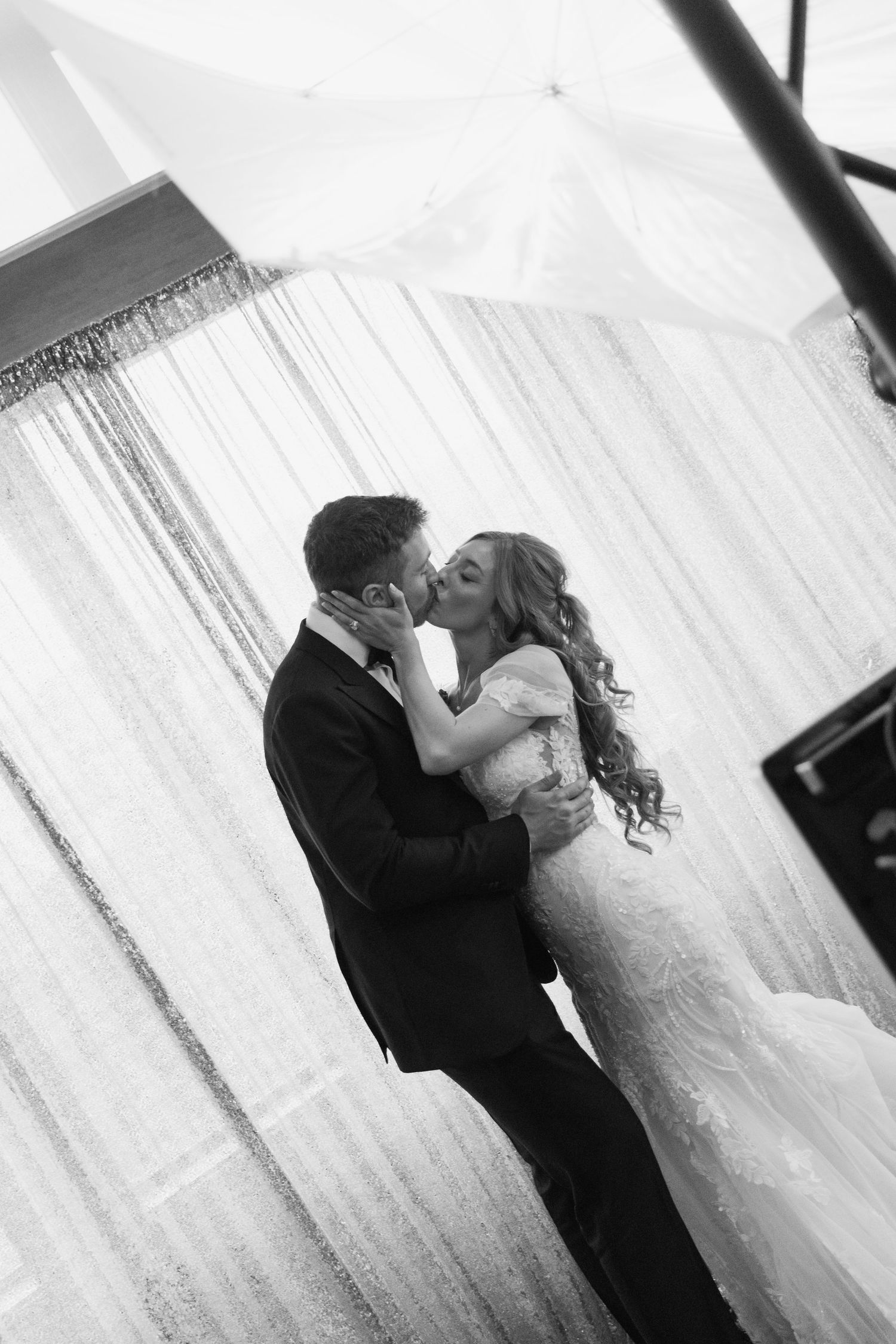Black and white photo of a bride and groom sharing a romantic kiss at their wedding reception.
