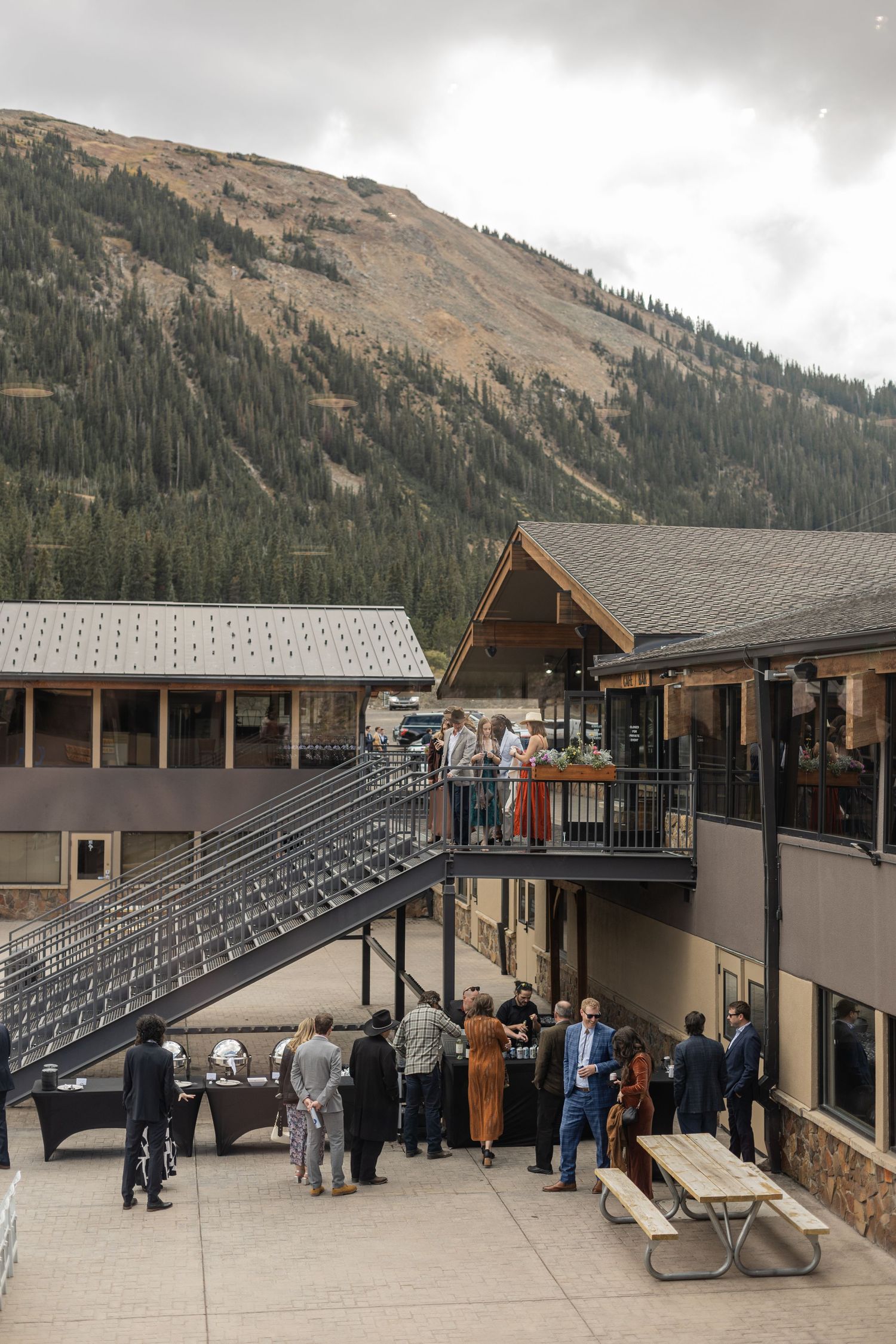 A panoramic view of a mountain lodge with outdoor seating and bleacher-style stadium seating against a scenic mountain backdrop.