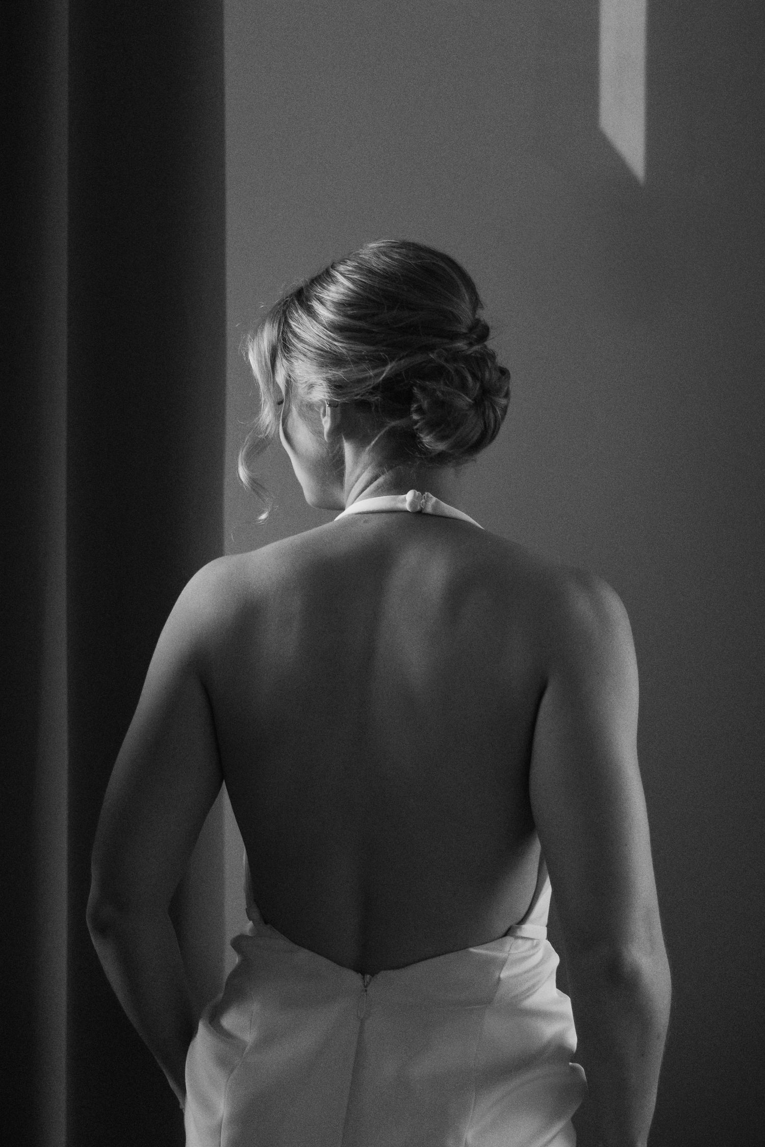 Black and white photo of a bride in a backless halter wedding gown with elegant updo hairstyle.