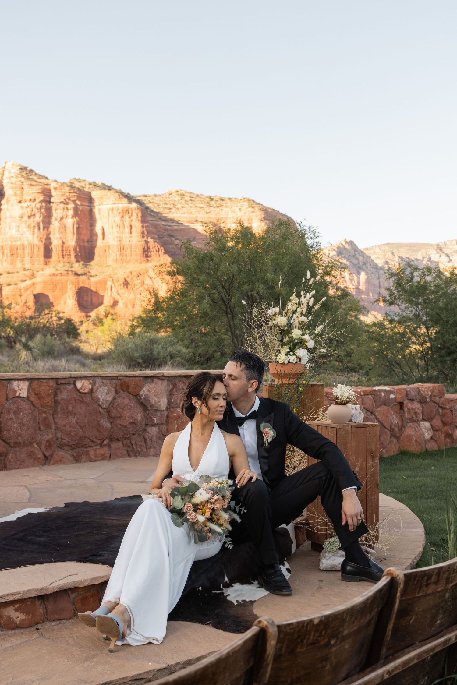 Newlyweds sit together at a scenic overlook with majestic red rock formations of Sedona at sunset.