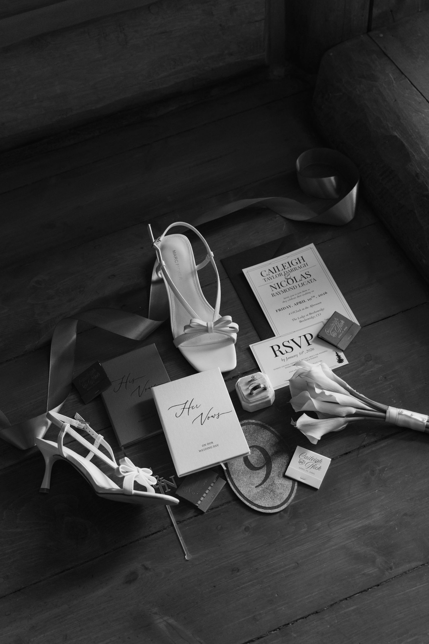 Black and white flat lay of wedding details including heels, invitations, RSVP card, rings, and bouquet on wooden steps.