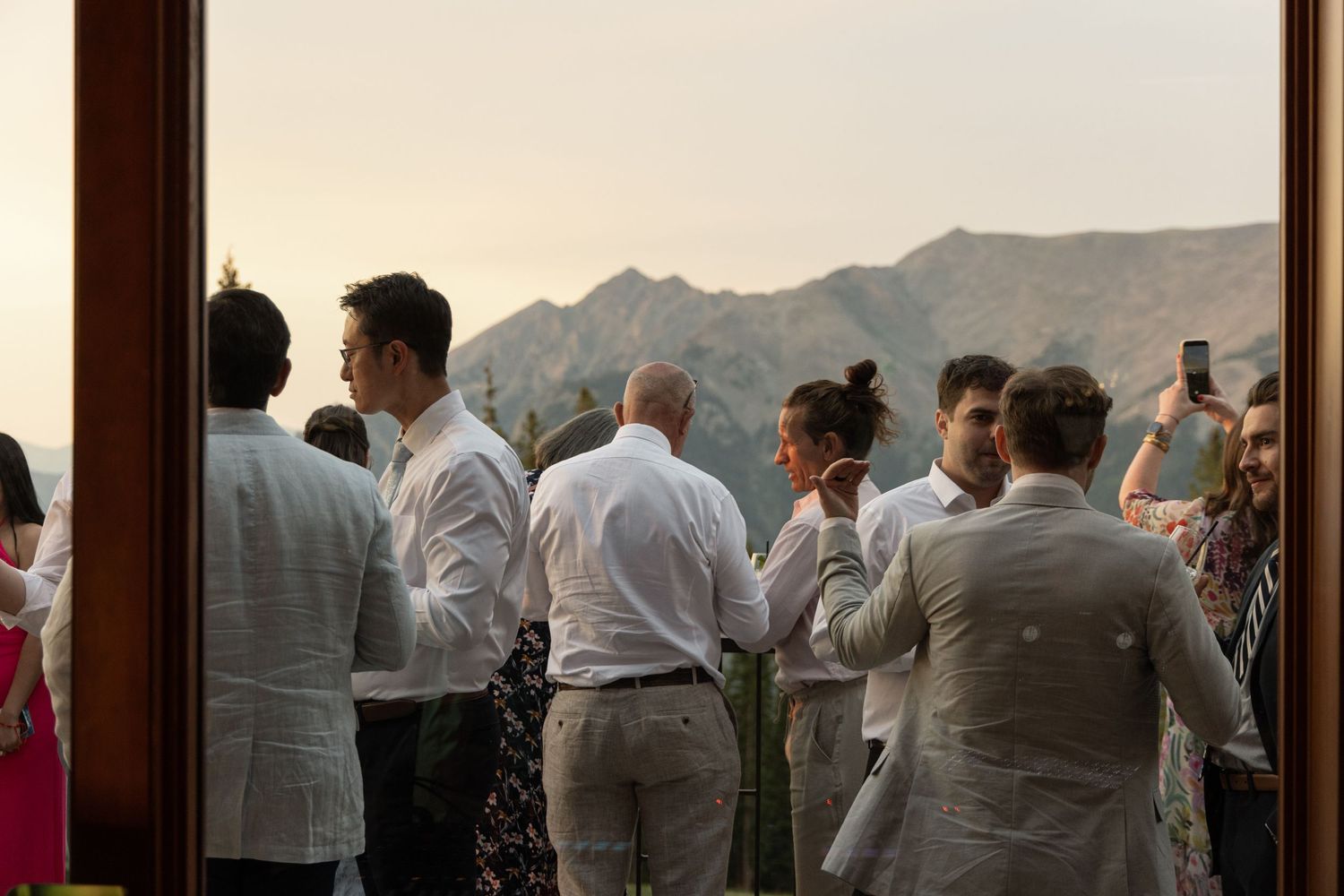 Elegant outdoor wedding reception guests in white attire enjoying mountain sunset views at a scenic venue.