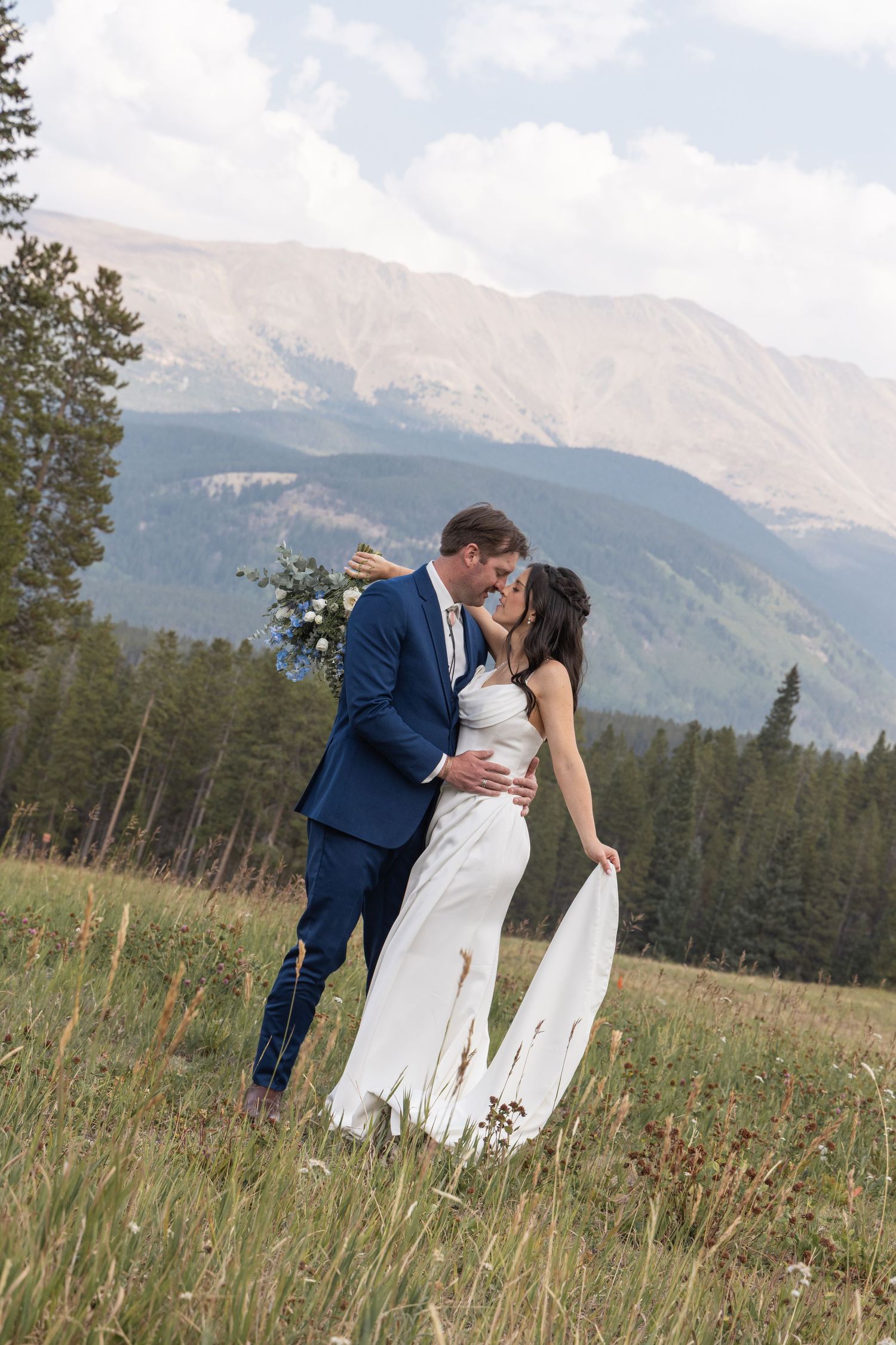 A romantic mountain wedding shoot in wildflower meadow with pine forest and majestic peaks in the background.