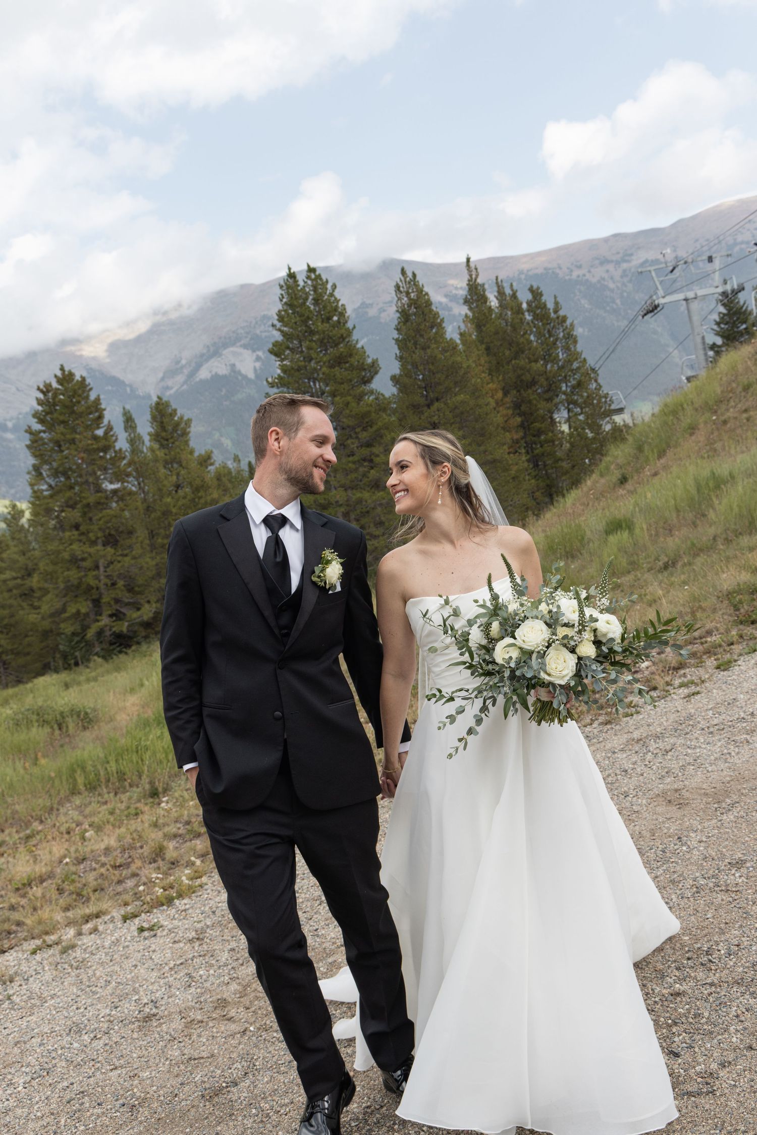 A couple shares a joyful moment on a mountainside during their wedding photoshoot with scenic mountain views.