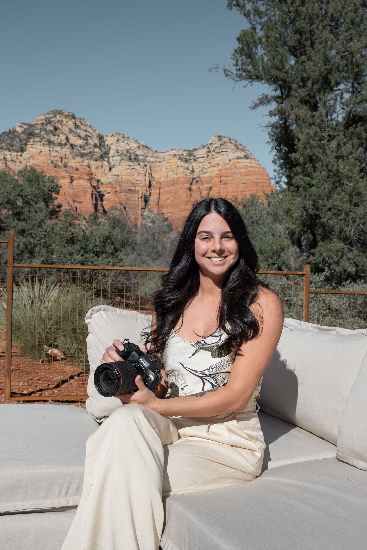 Person in white dress sits on outdoor couch with stunning red rock formations of Sedona visible in background.