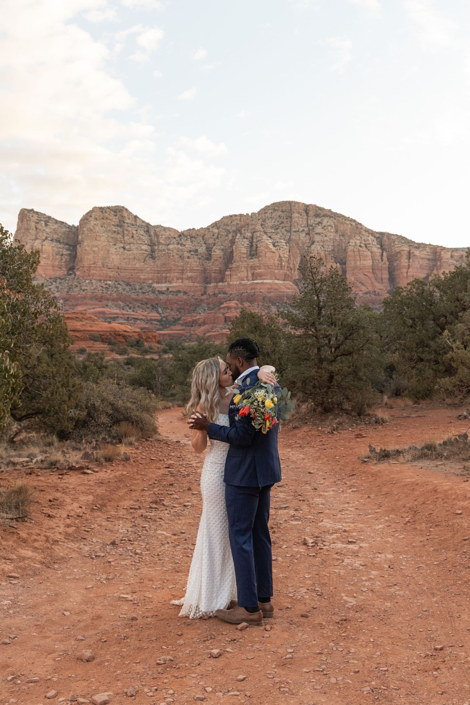 A couple in wedding attire embraces against the stunning backdrop of red rock formations in Sedona, Arizona.
