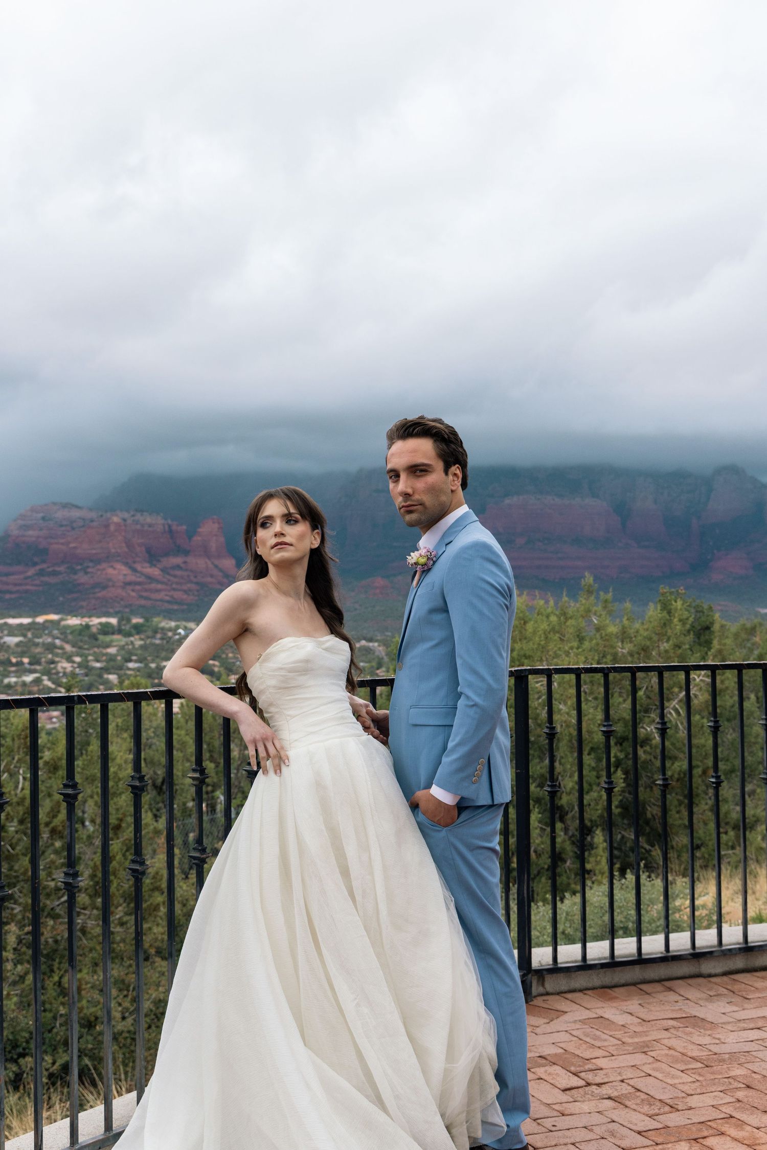 Wedding couple poses on a terrace overlooking the red rock formations and scenic landscape of Sedona, Arizona.