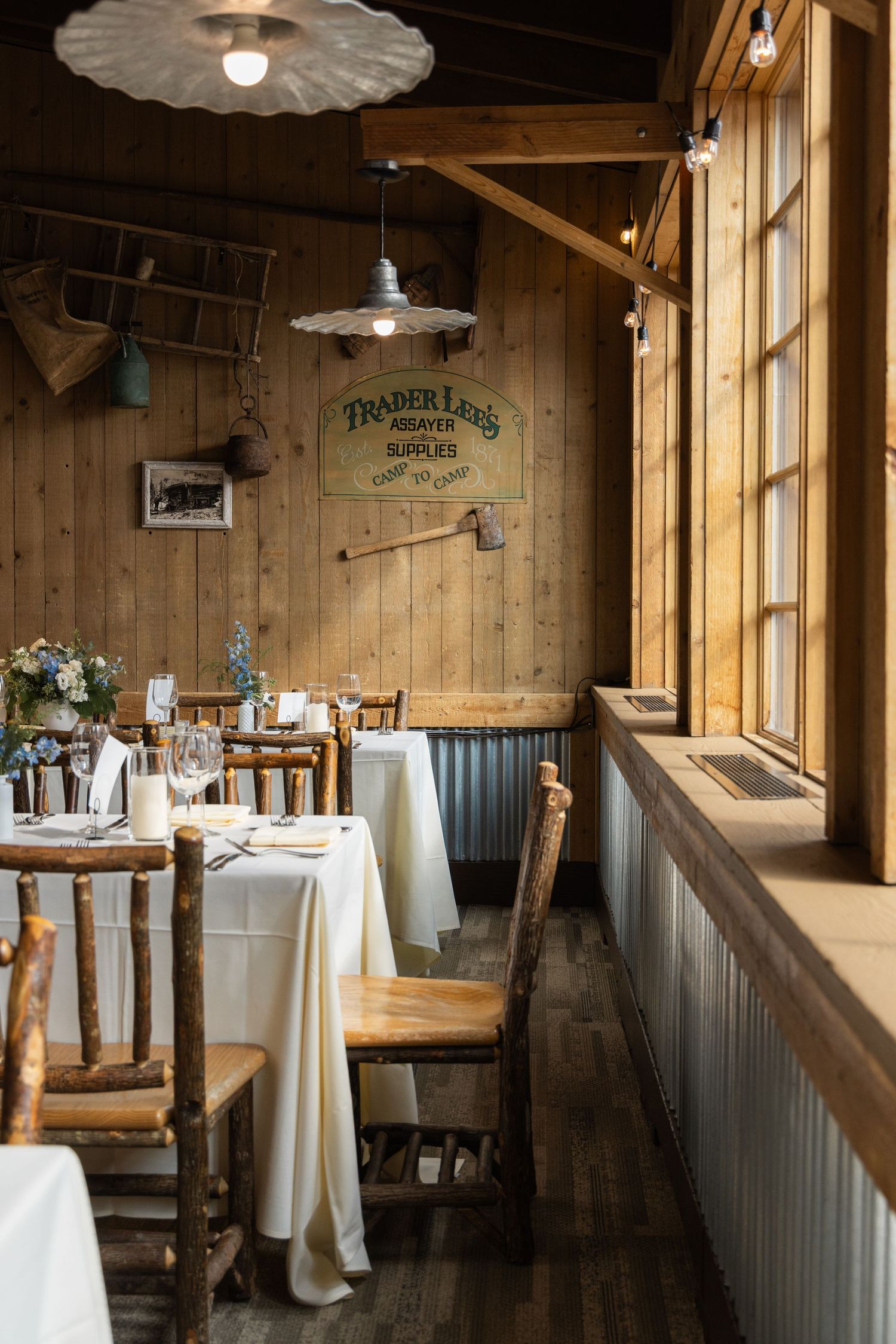Rustic wooden restaurant interior with white tablecloths and wainscoting features warm lighting and panoramic windows.