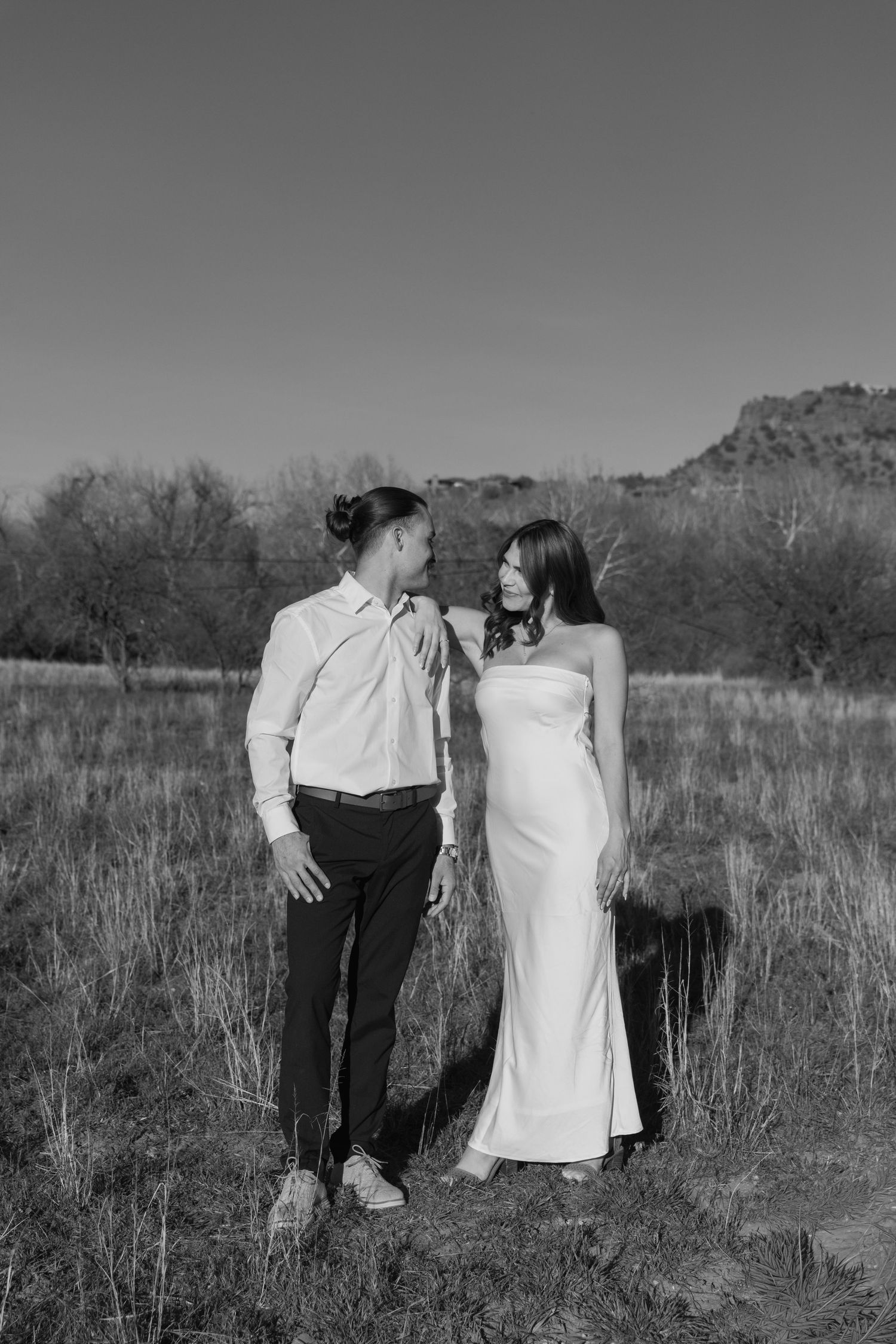 A romantic black and white photo of a couple in formal attire standing together in a desert landscape.