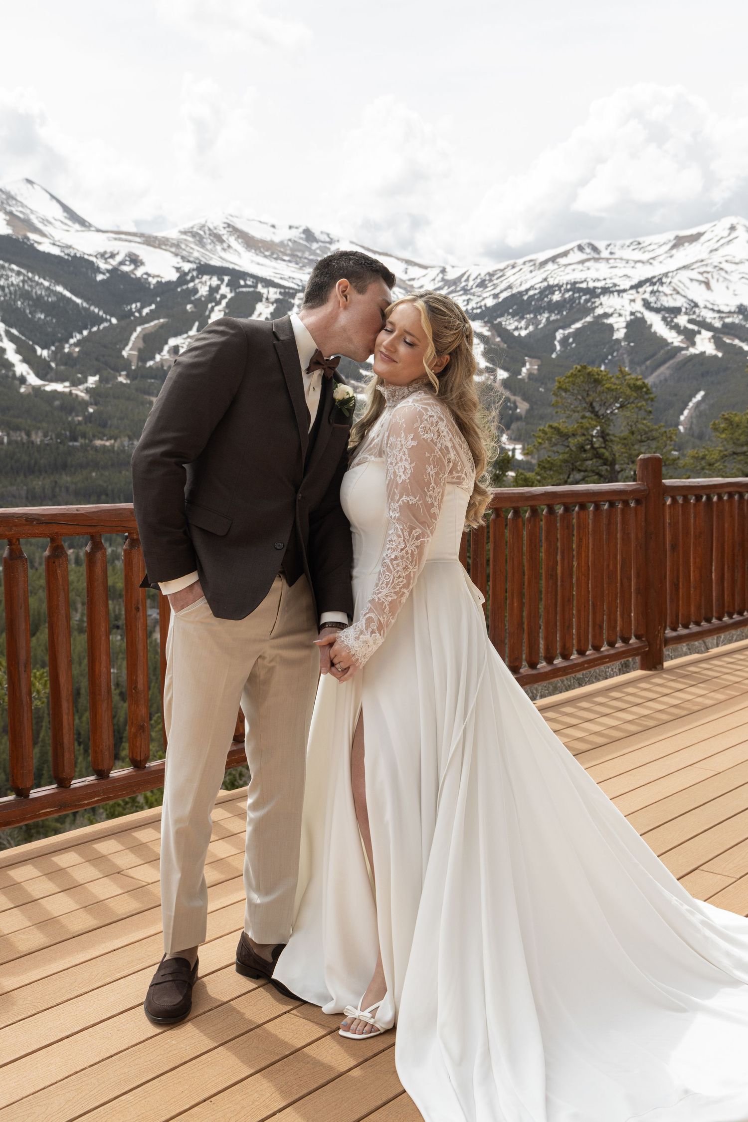 Bride and groom share a romantic moment on a mountain deck with snowy peaks backdrop at their Colorado wedding.