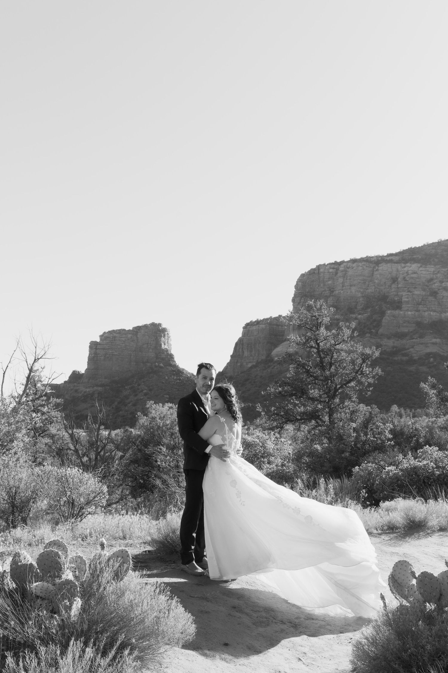 Black and white photo of bride and groom embracing in Sedona desert landscape with red rock formations.