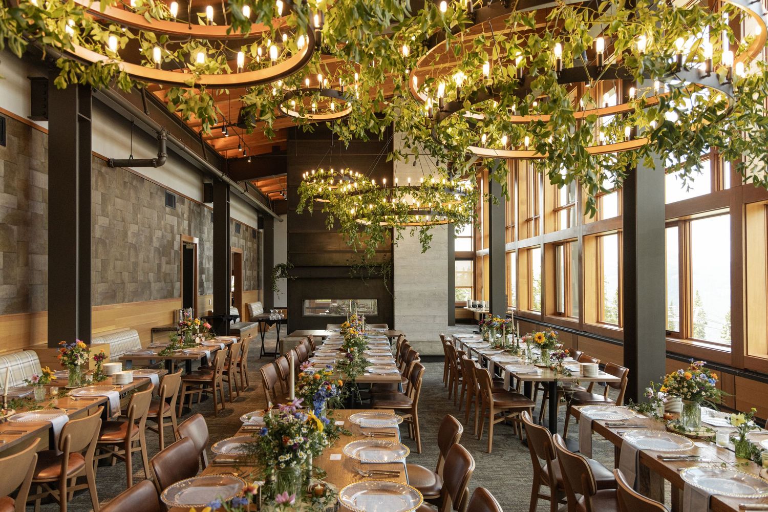 Elegant restaurant dining room with circular greenery chandeliers, wooden tables, and large windows creating a botanical ambiance.