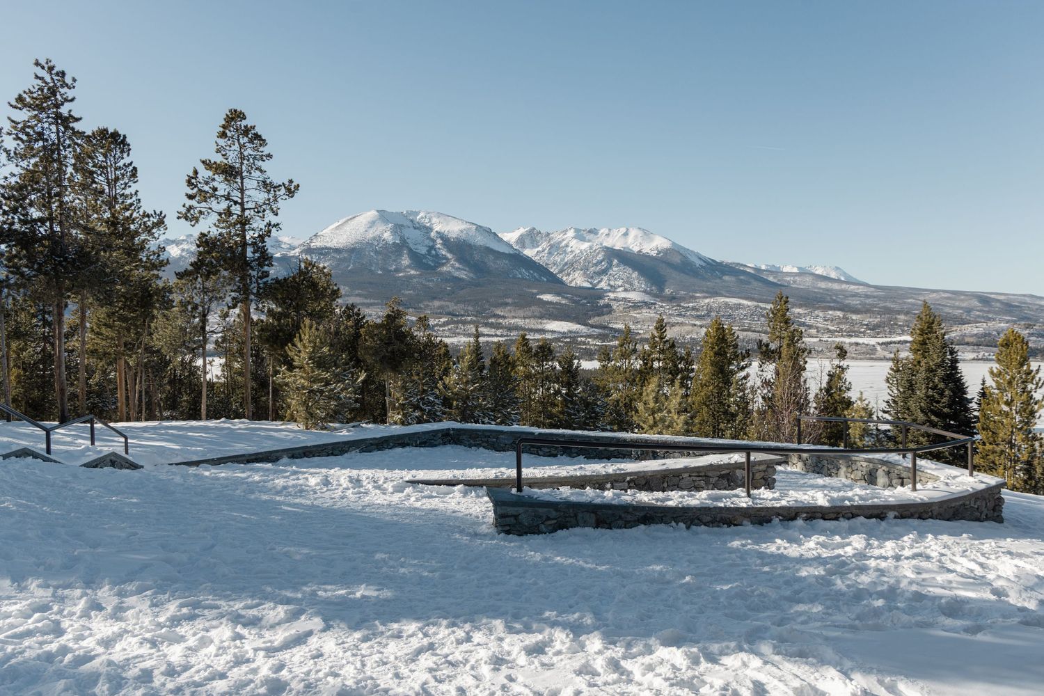 Snow-covered mountain peaks rise above a winter forest landscape with evergreen trees in the foreground.