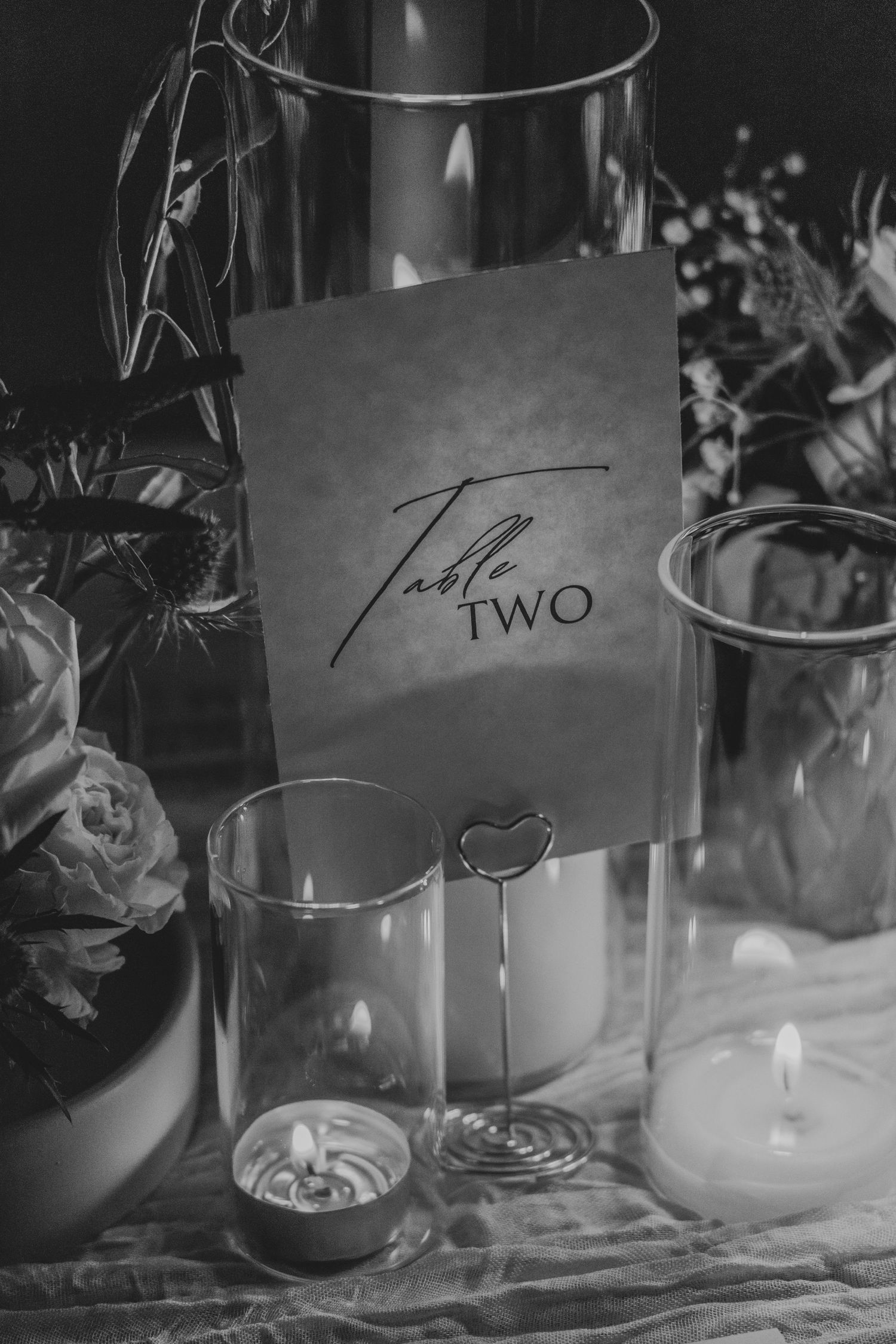 Black and white table setting with candles and a handwritten table number card creates an elegant dining atmosphere.
