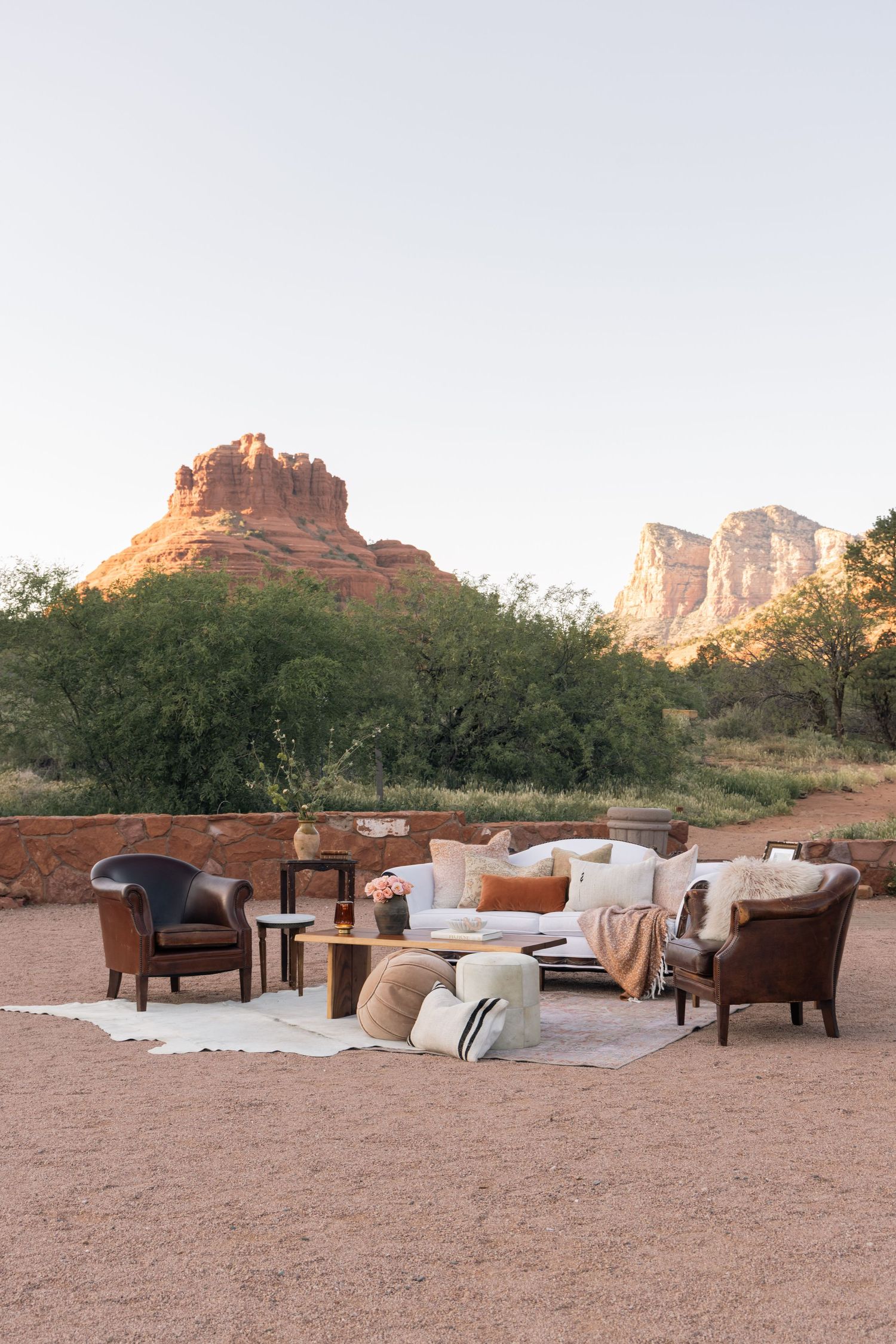Outdoor lounge seating with leather chairs and white sofa set against Sedona red rock formations at dusk.