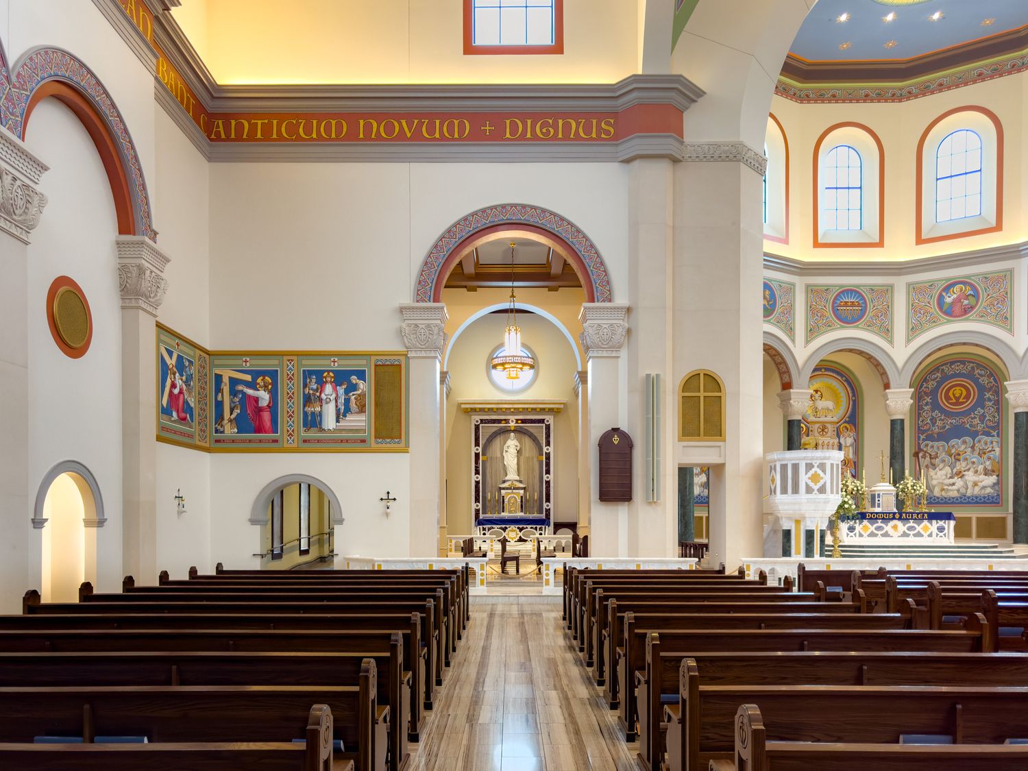 Ornate Catholic church interior with wooden pews, colorful murals, arched ceilings, and a decorative altar in a grand nave.