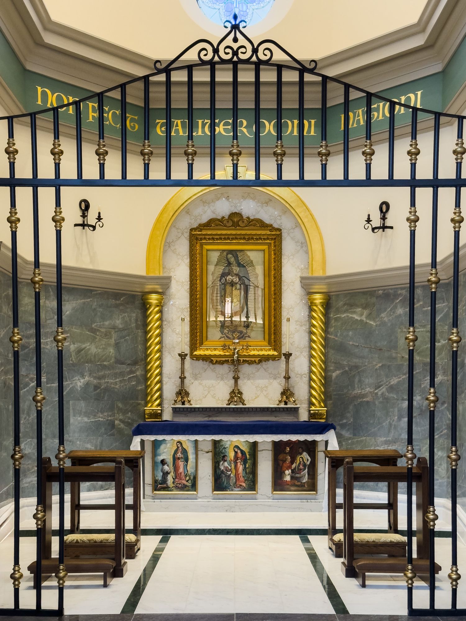 Ornate Catholic chapel altar with gilded ironwork gate, Virgin Mary statue in golden frame, and marble walls.