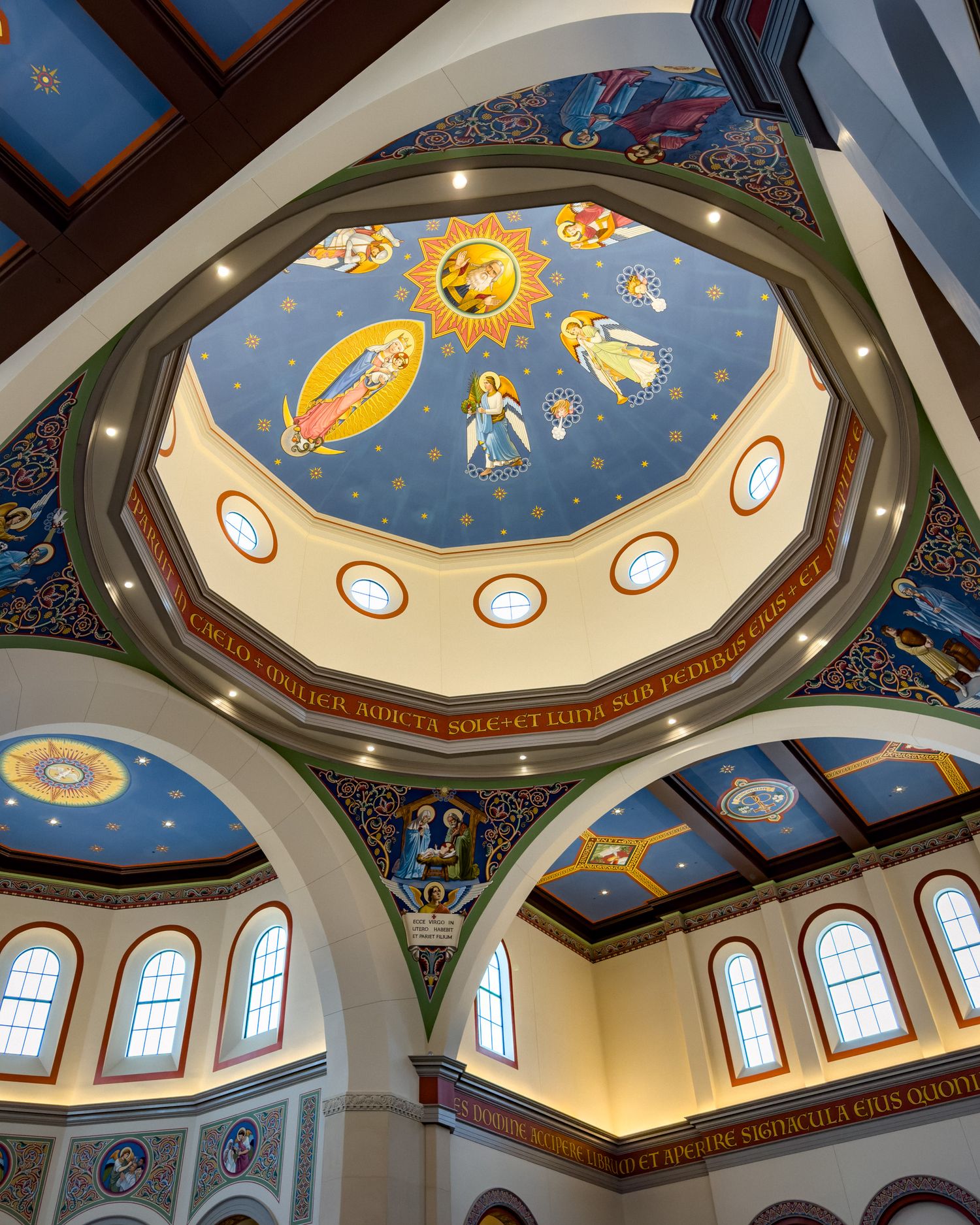 Ornate church dome ceiling with blue sky mural, golden sun, angels, and colorful religious iconography in a Byzantine style.