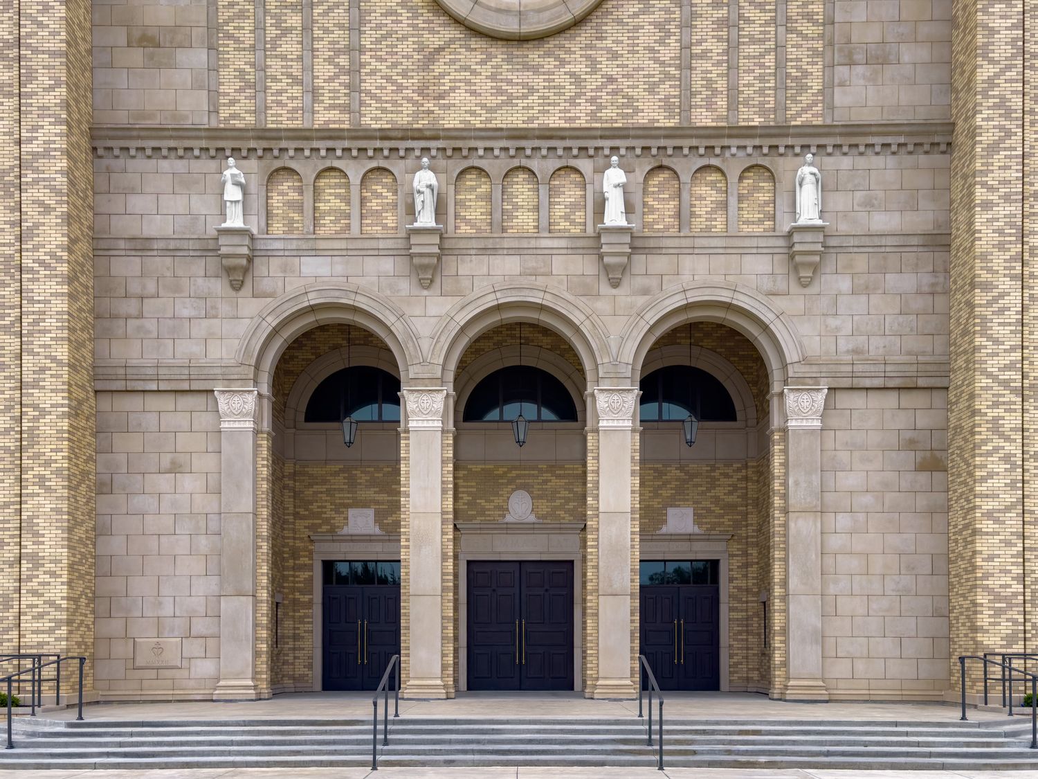 Grand stone church facade with three arched doorways, ornate carvings, statues, and wide steps in classical architecture.