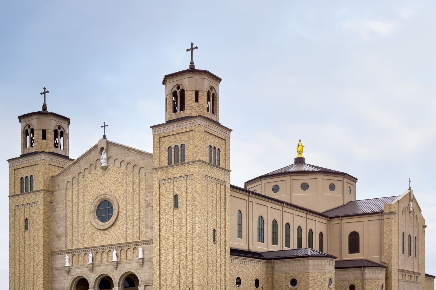 Large ornate church with twin bell towers, rose window, and golden dome under a cloudy sky.