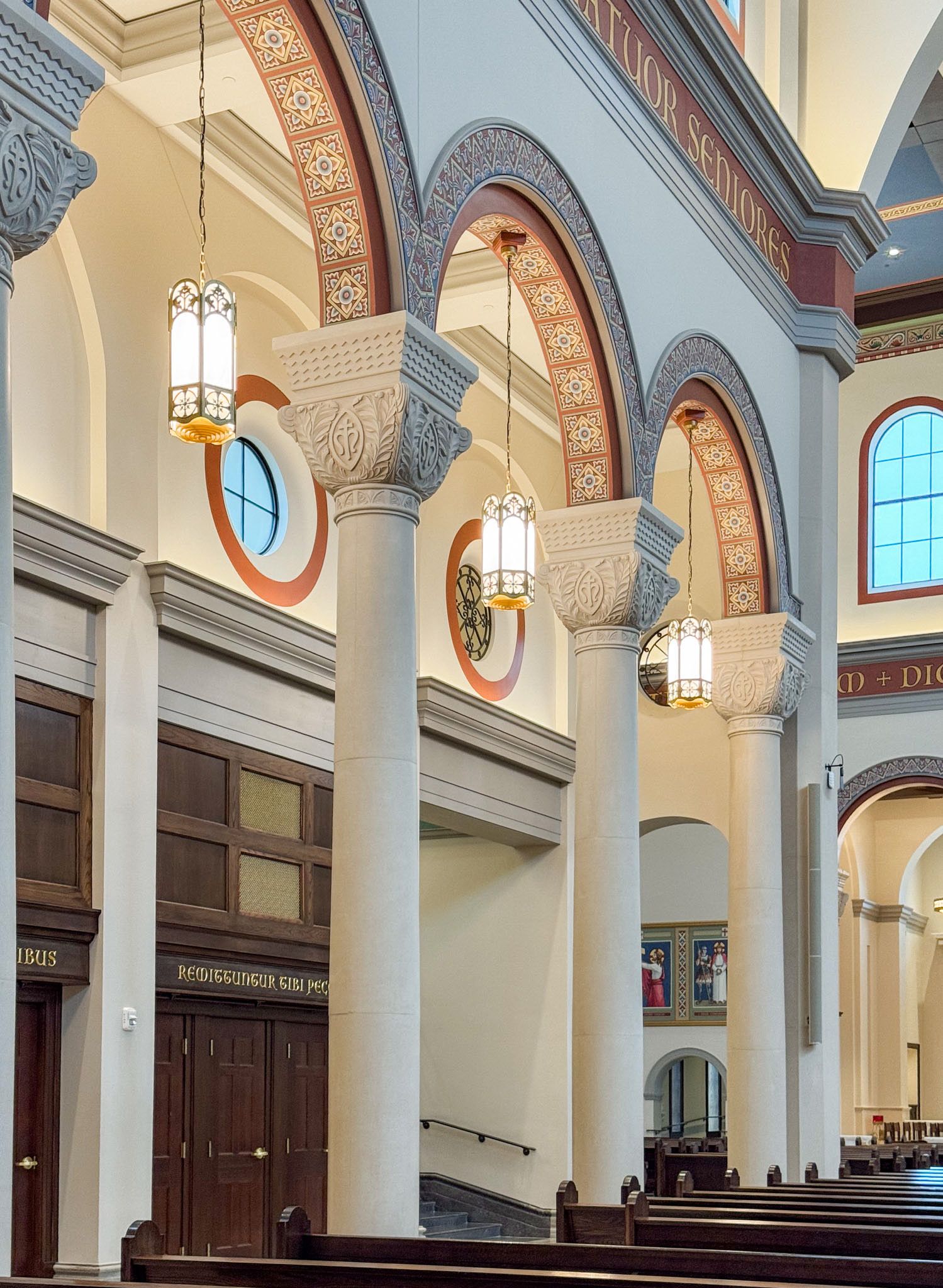 Ornate church interior with tall white columns, decorative arches, hanging lanterns, and wooden pews in a grand cathedral.