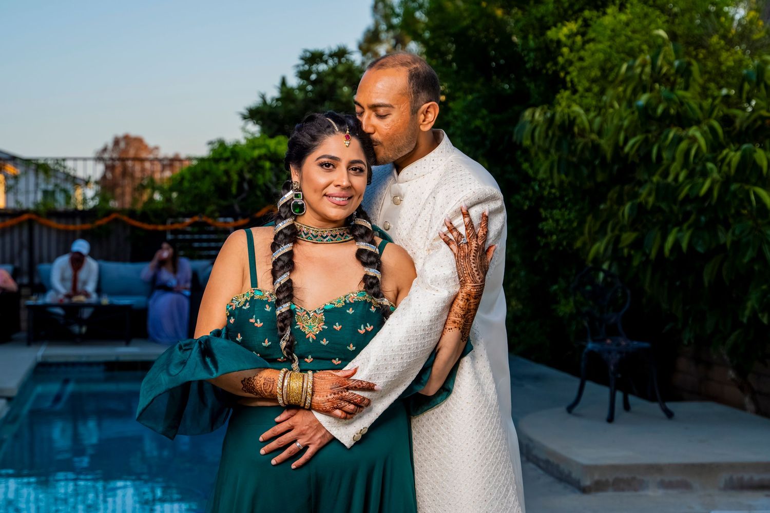 Couple in traditional formal attire embracing by a pool at sunset. riverside.