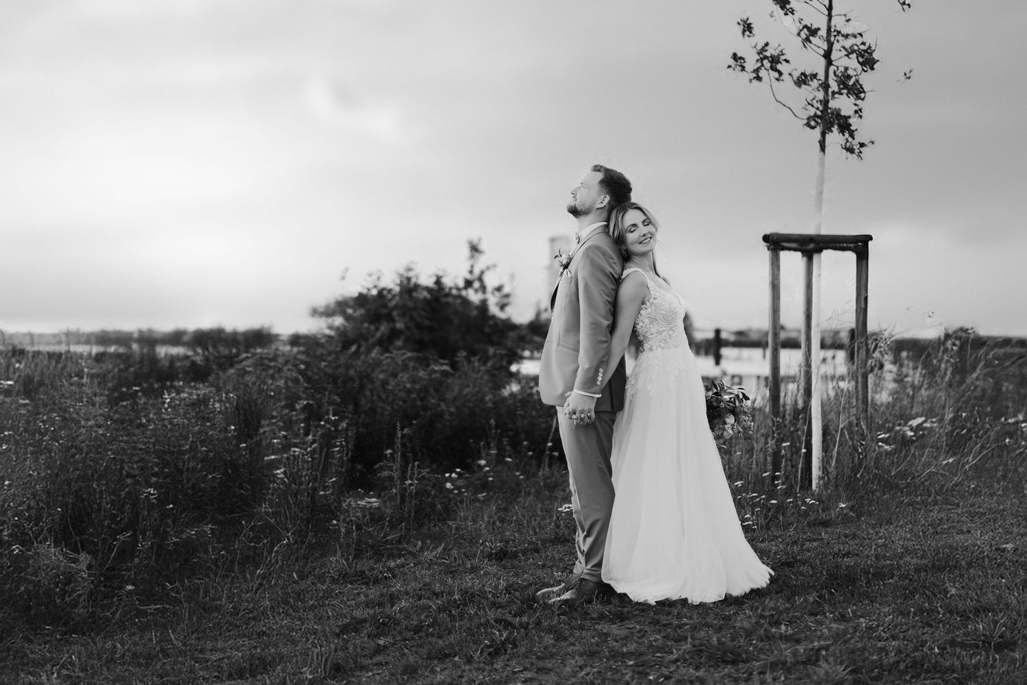 Black and white photo of bride and groom standing back-to-back in an open field at dusk.