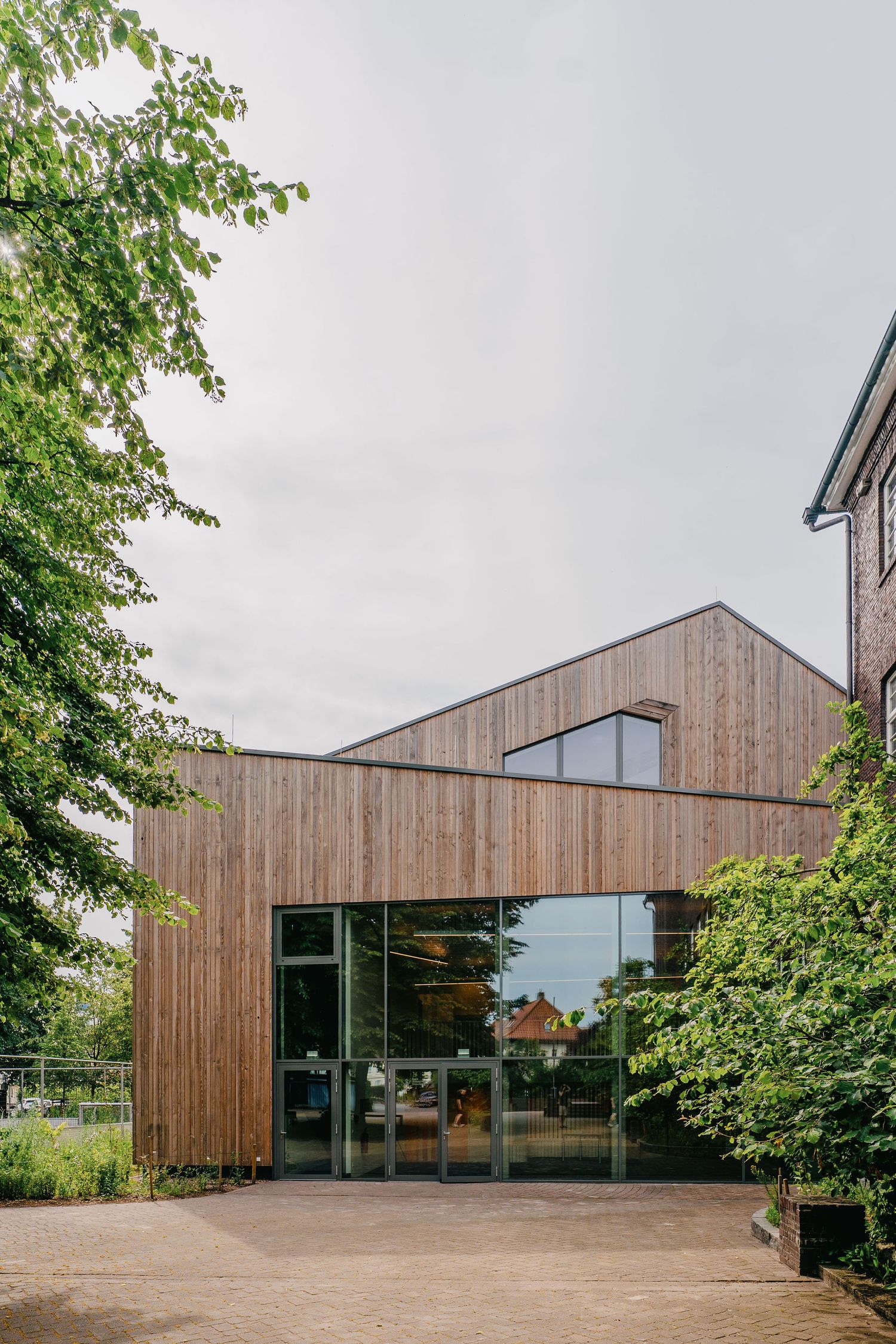 Modern wooden facade building with glass entrance doors surrounded by green trees.