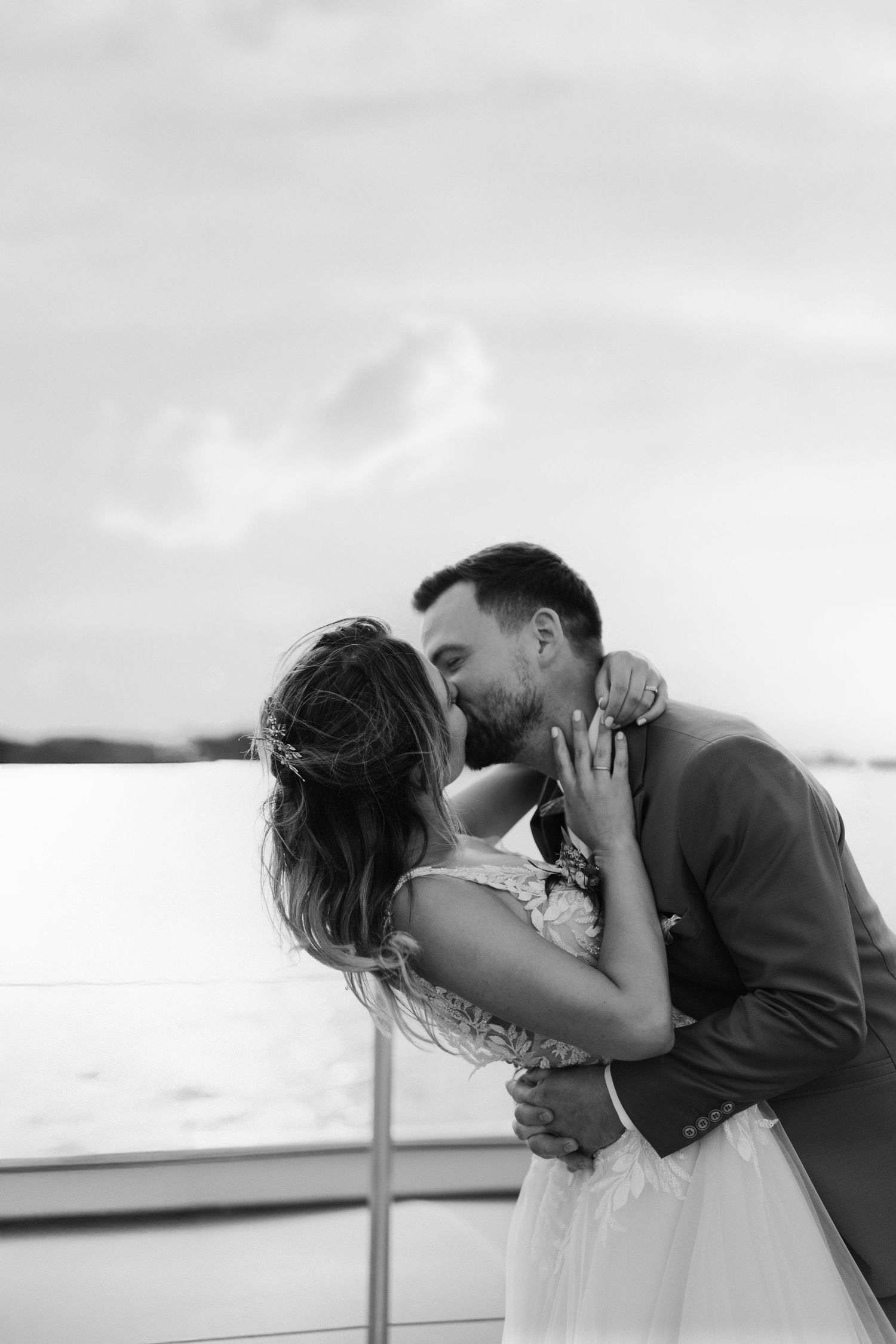 Black and white intimate photo of bride and groom sharing passionate kiss by the water.