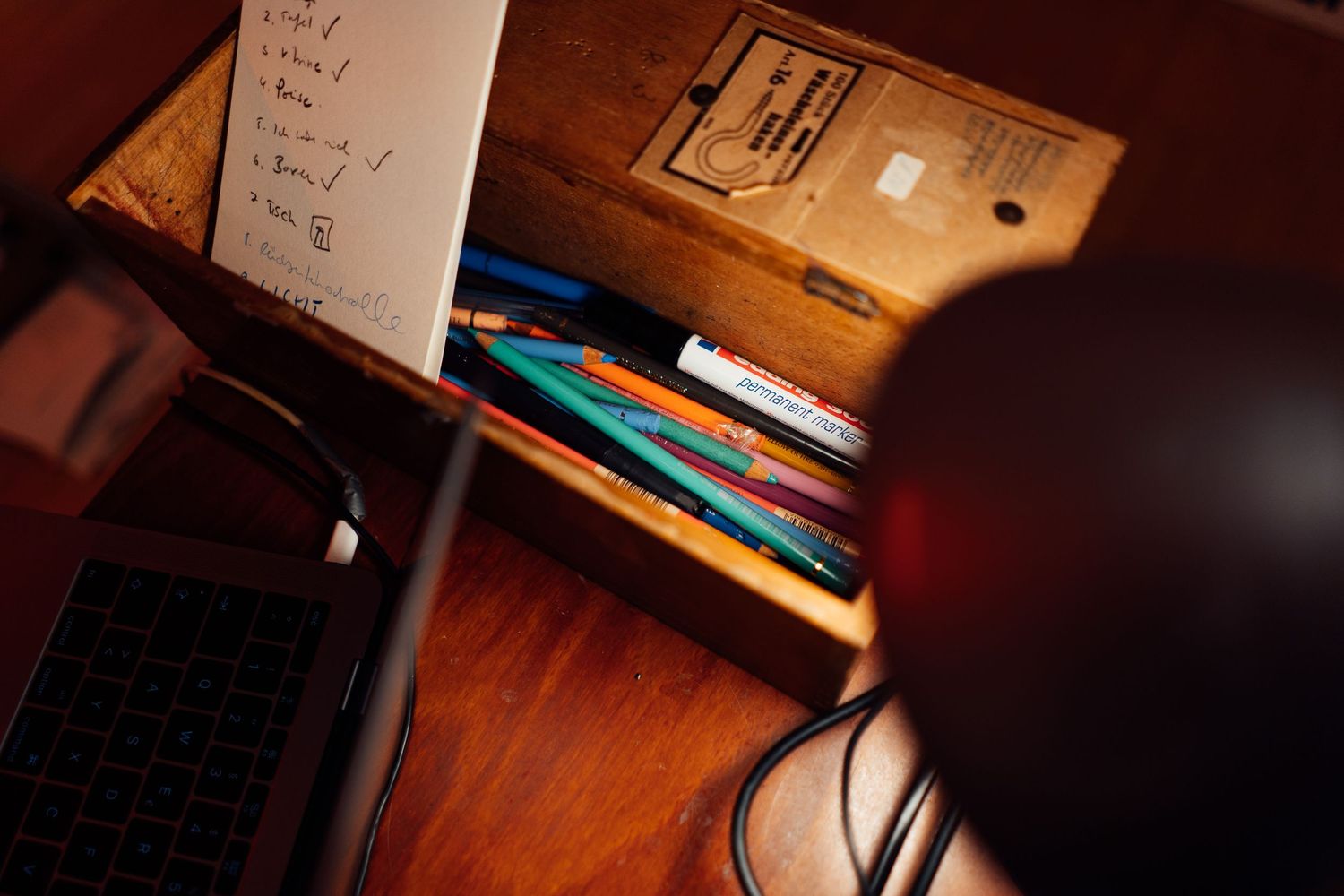 Overhead view of a wooden desk organizer with colorful pens, pencils, and handwritten notes.